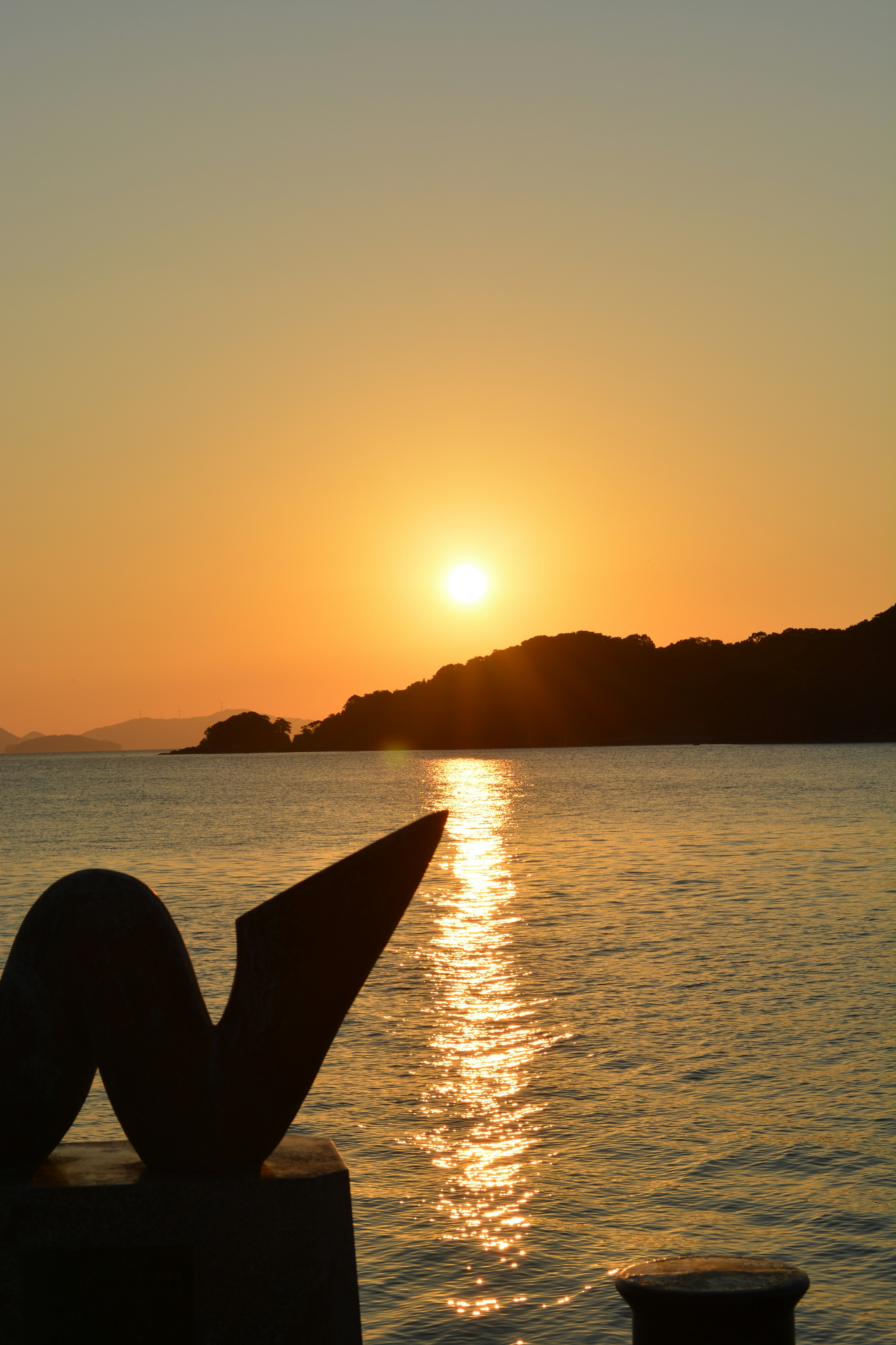 Hermoso atardecer reflejándose en el mar con una escultura en silueta