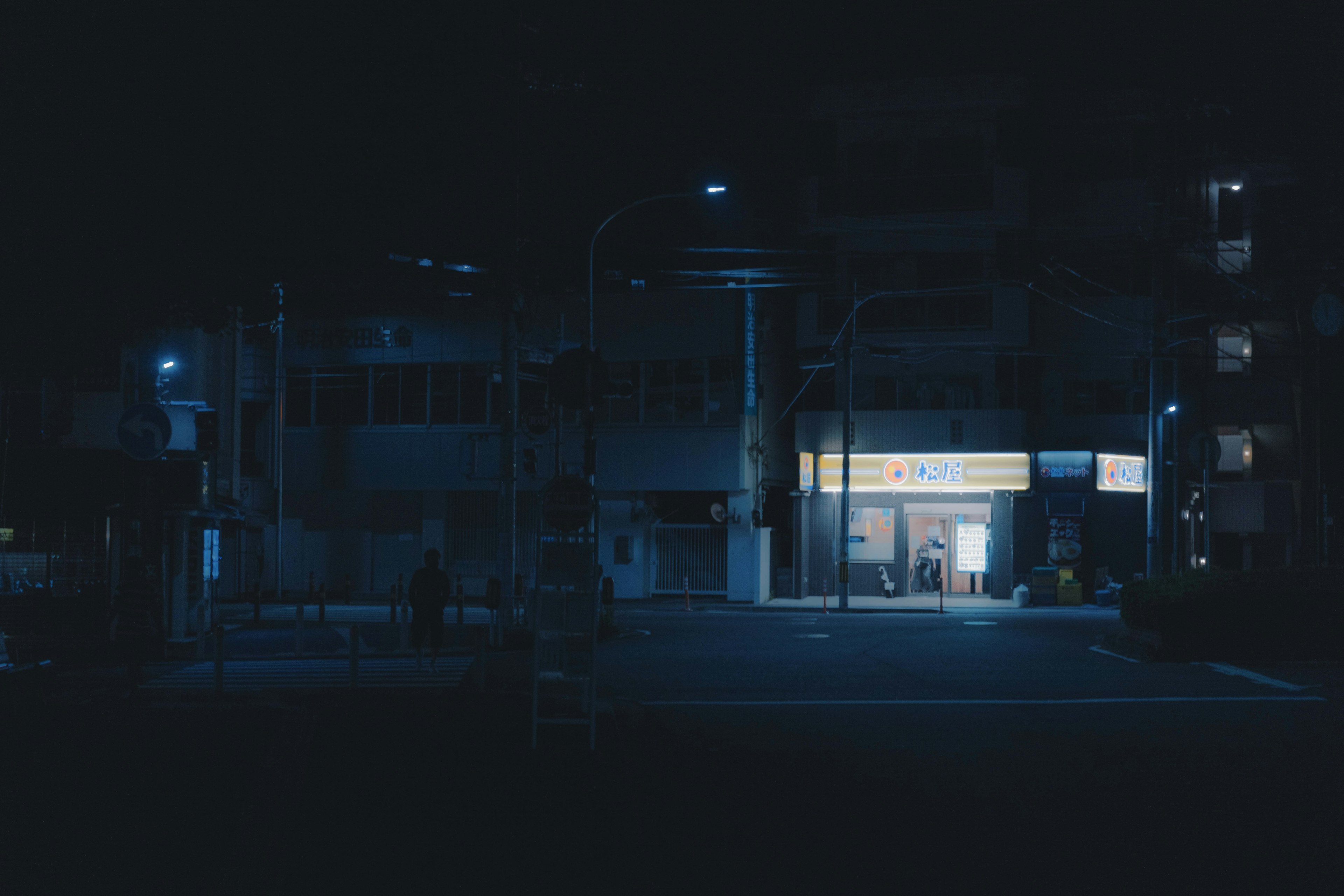 Escena nocturna con una tienda de conveniencia iluminada por luz azul