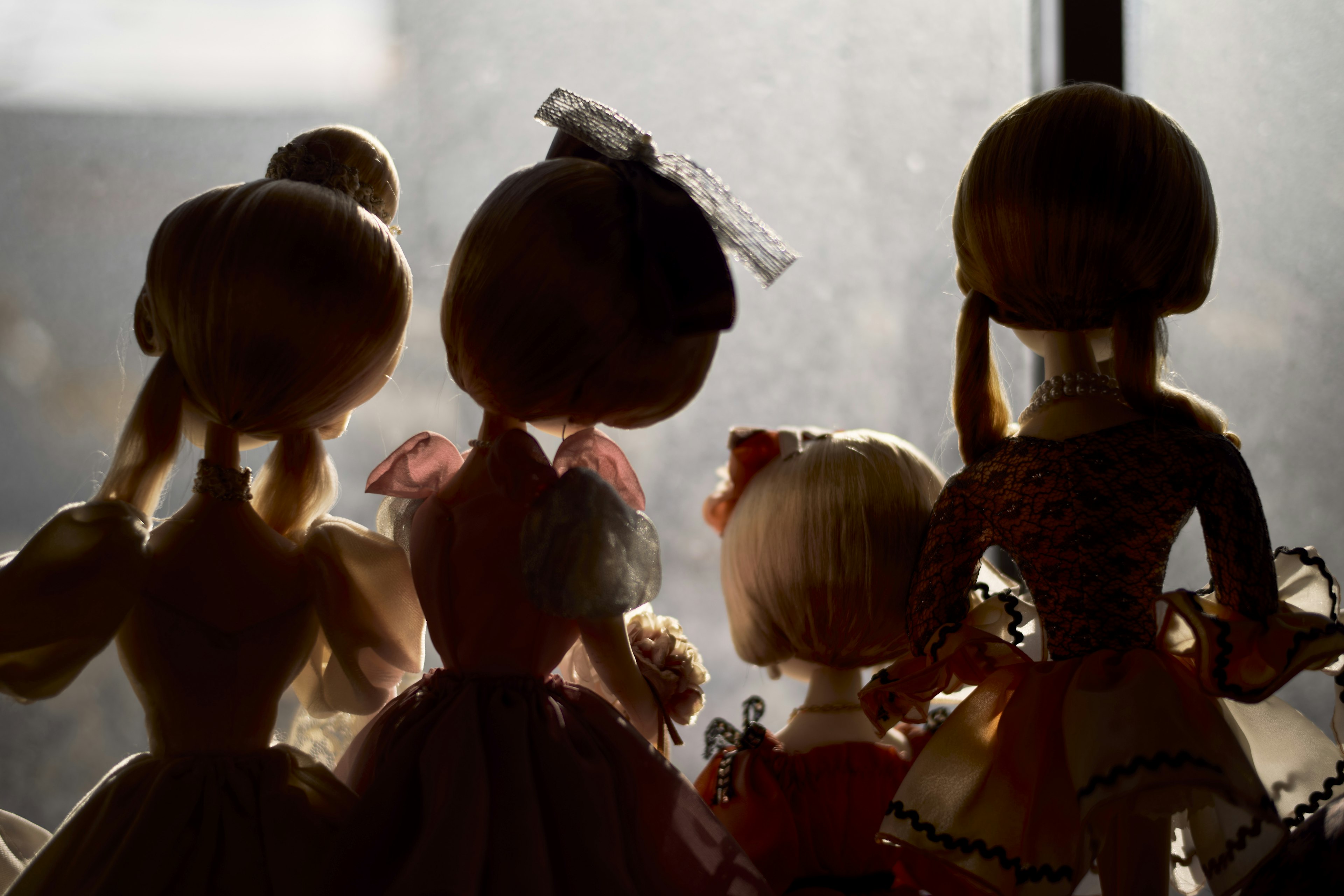 Silhouettes of dolls standing by a window featuring different outfits and hairstyles