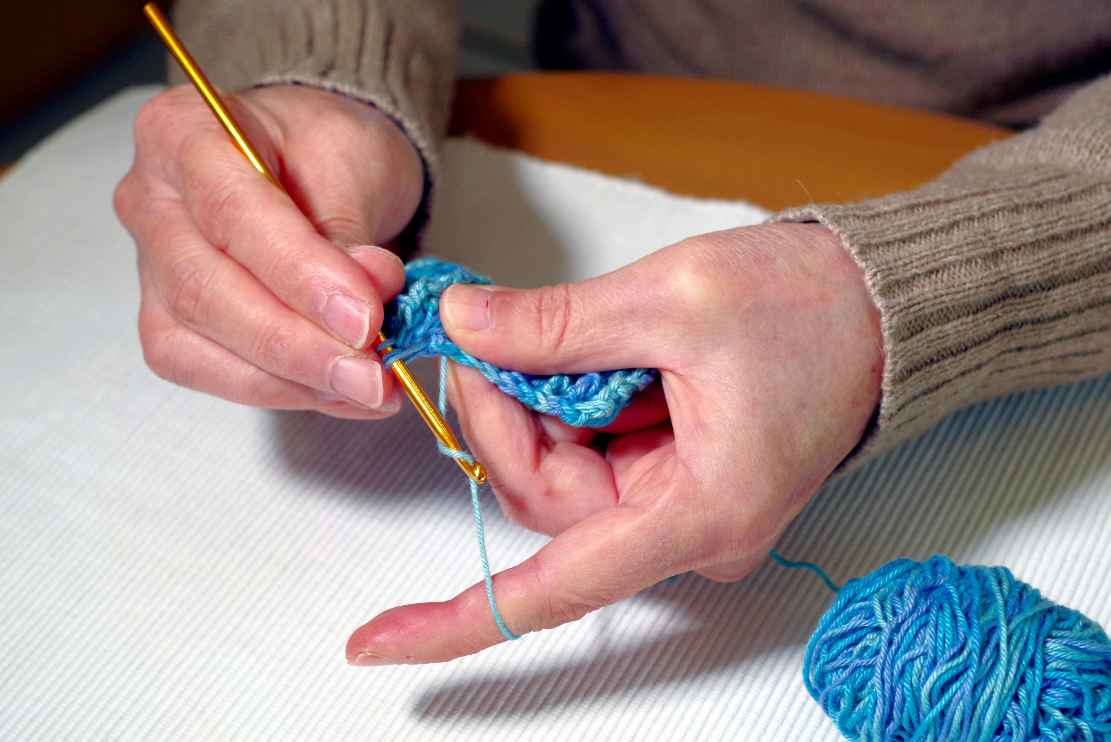 Mani che lavorano a uncinetto con filato blu