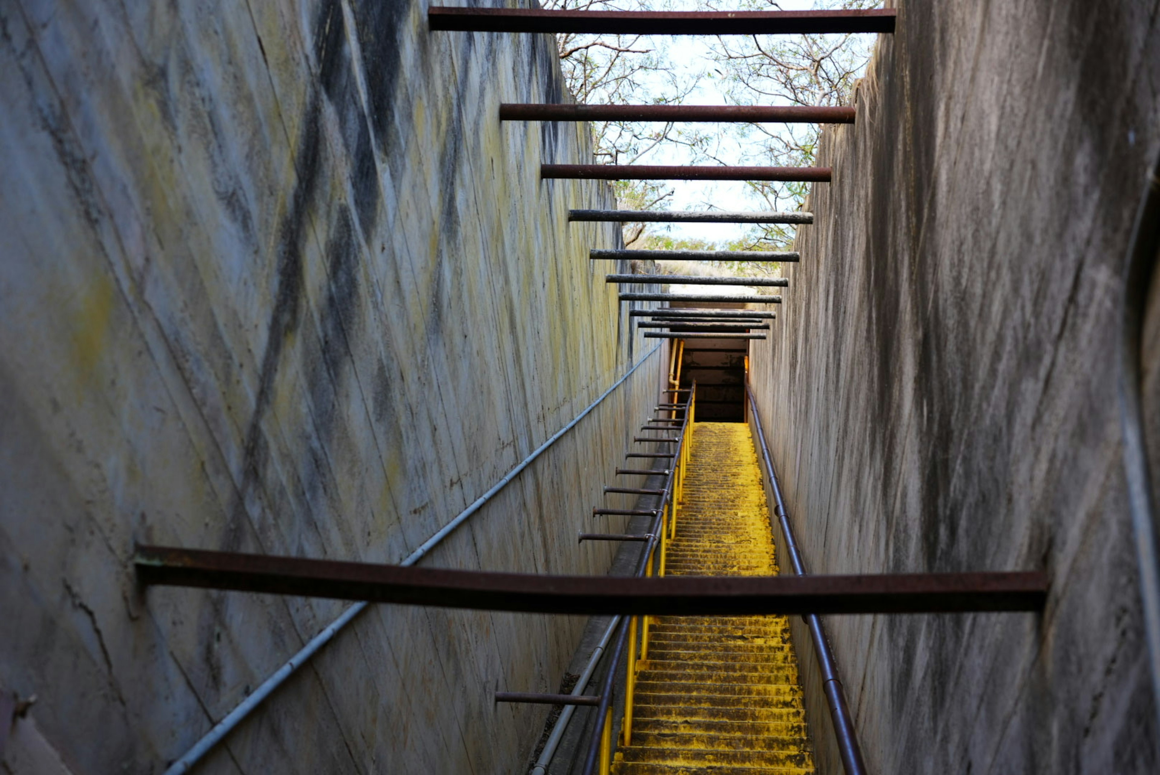 Blick von unten auf eine Treppe mit gelben Stufen Betonsäulen und Metallgeländern