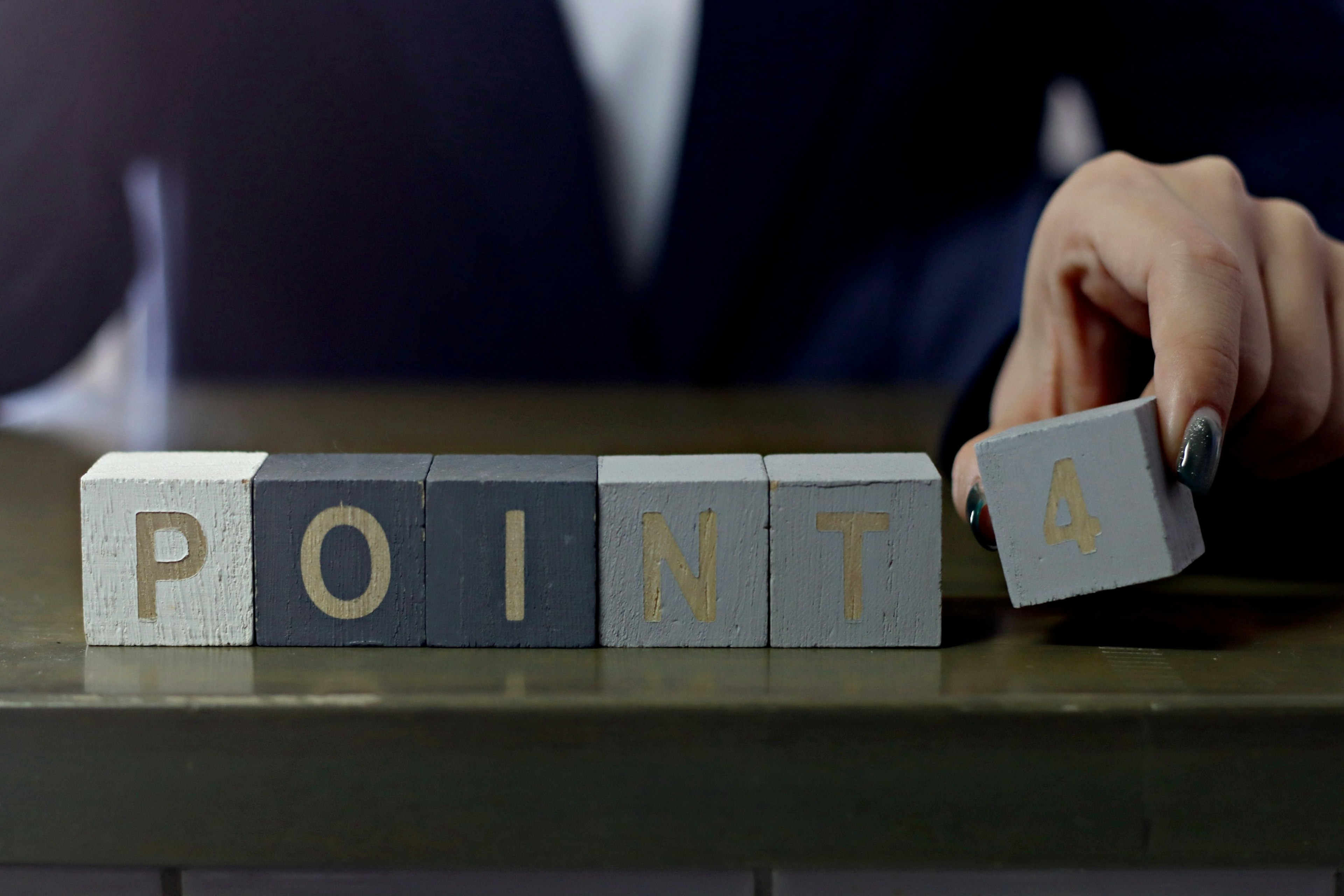 Eine Person in einem Anzug zeigt das Wort 'POINT' mit Buchstabenblöcken