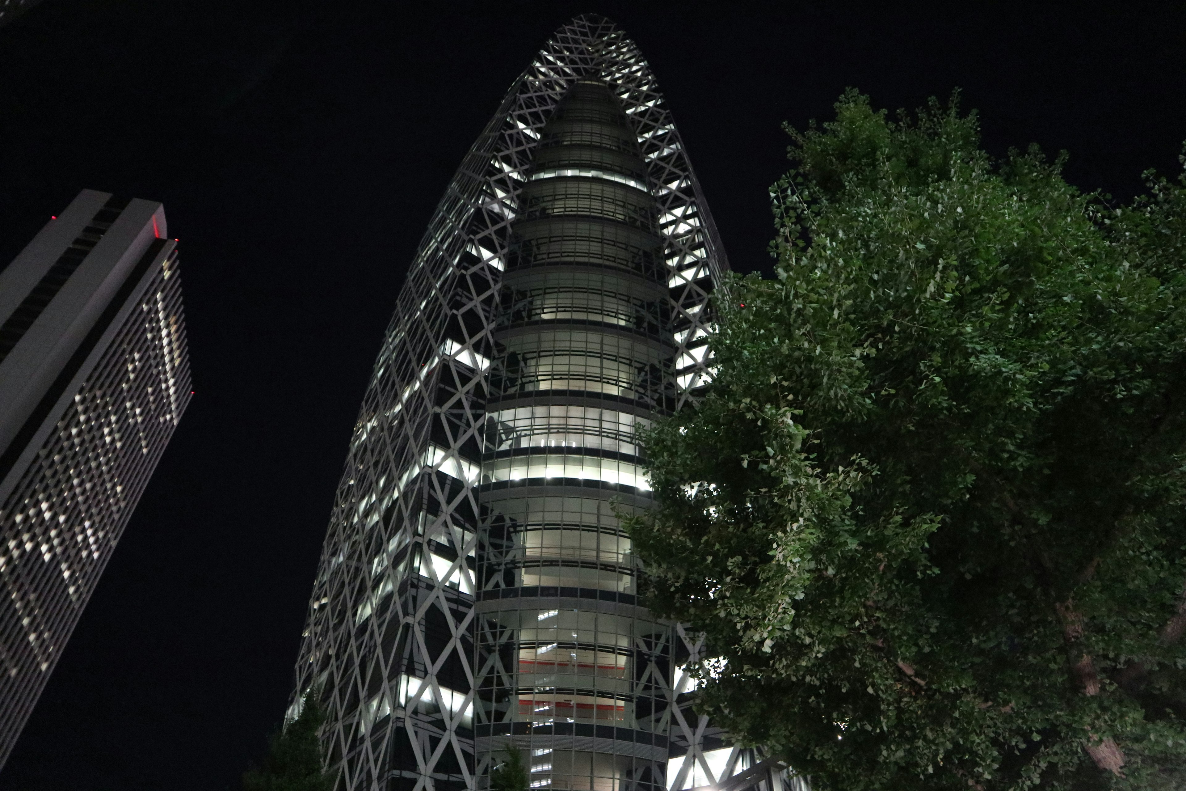 Die markante Form des Mode Gakuen Cocoon Tower bei Nacht mit umliegenden Bäumen