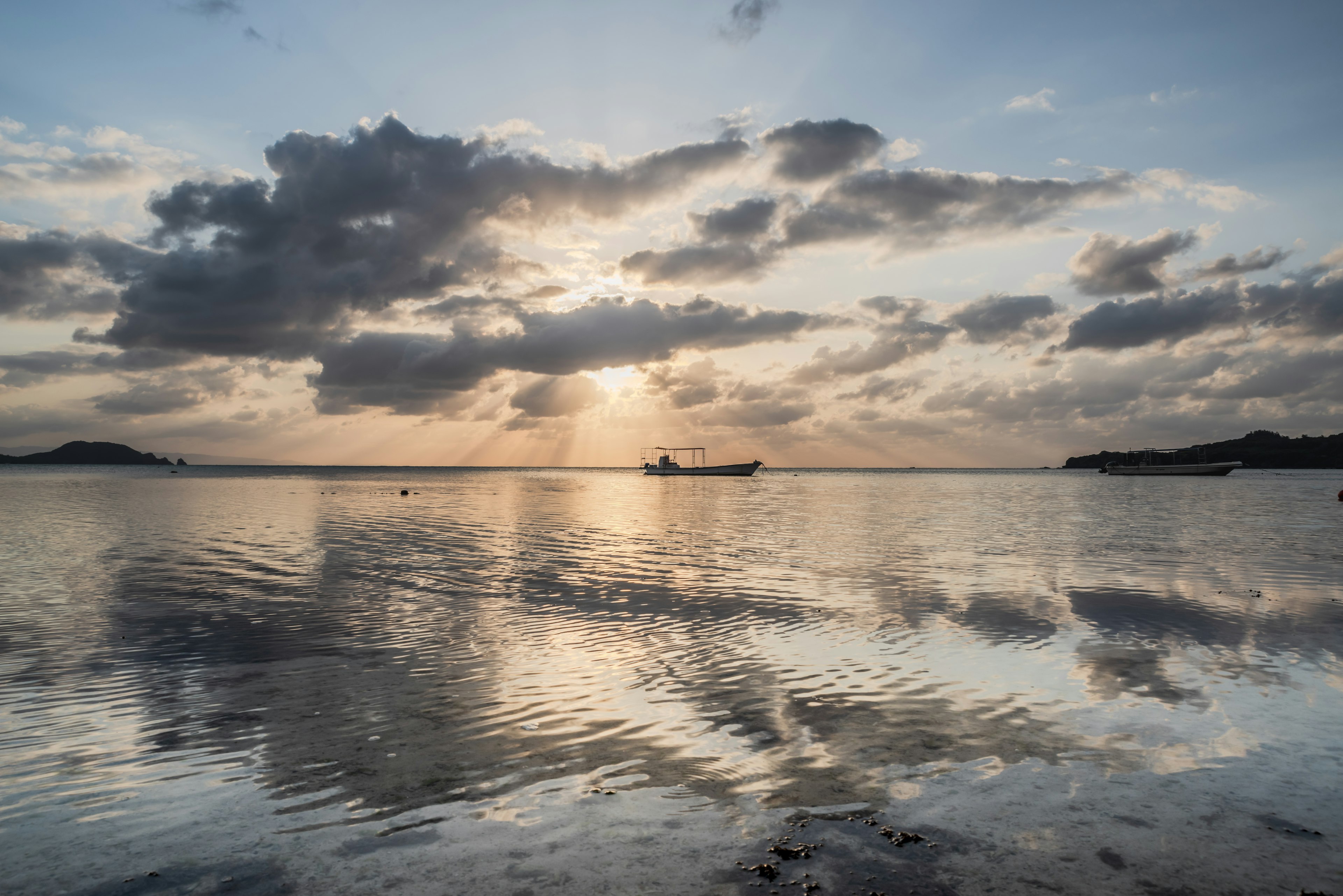 Fishing boat silhouetted against a sunset with clouds reflecting on calm water