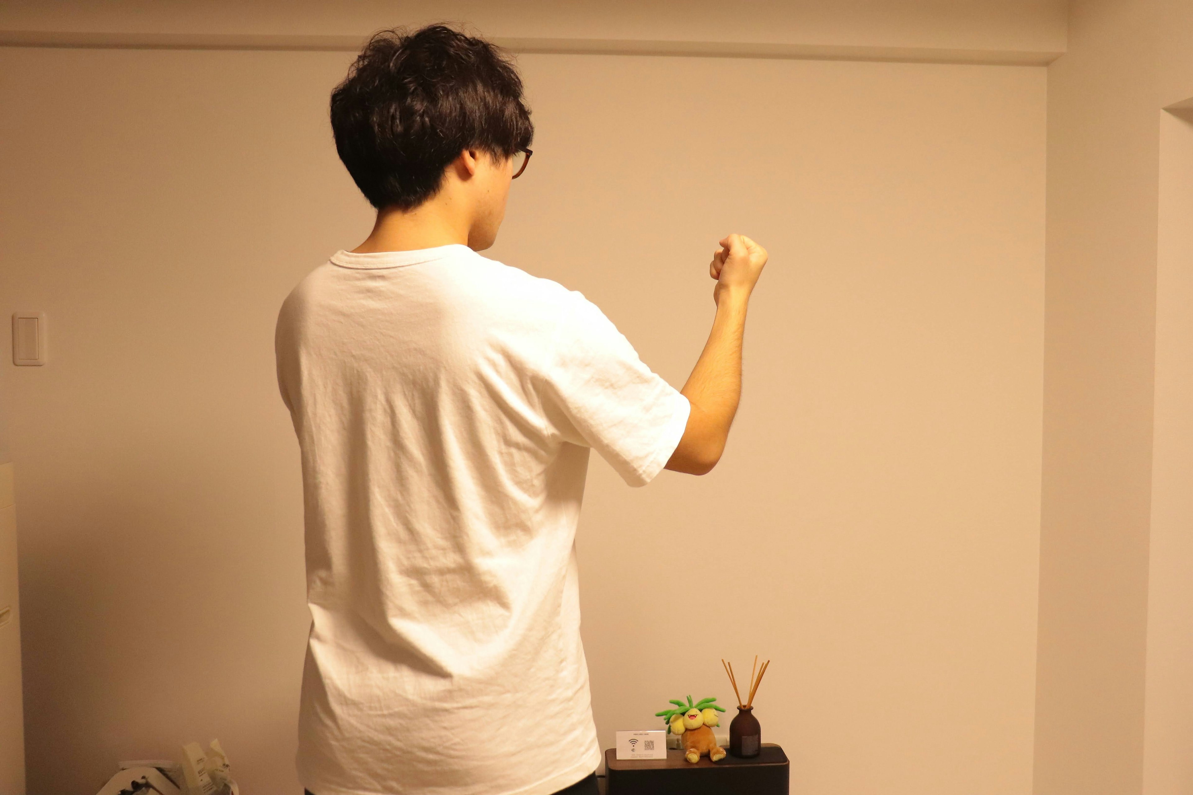 A man in a white t-shirt is gesturing towards a wall