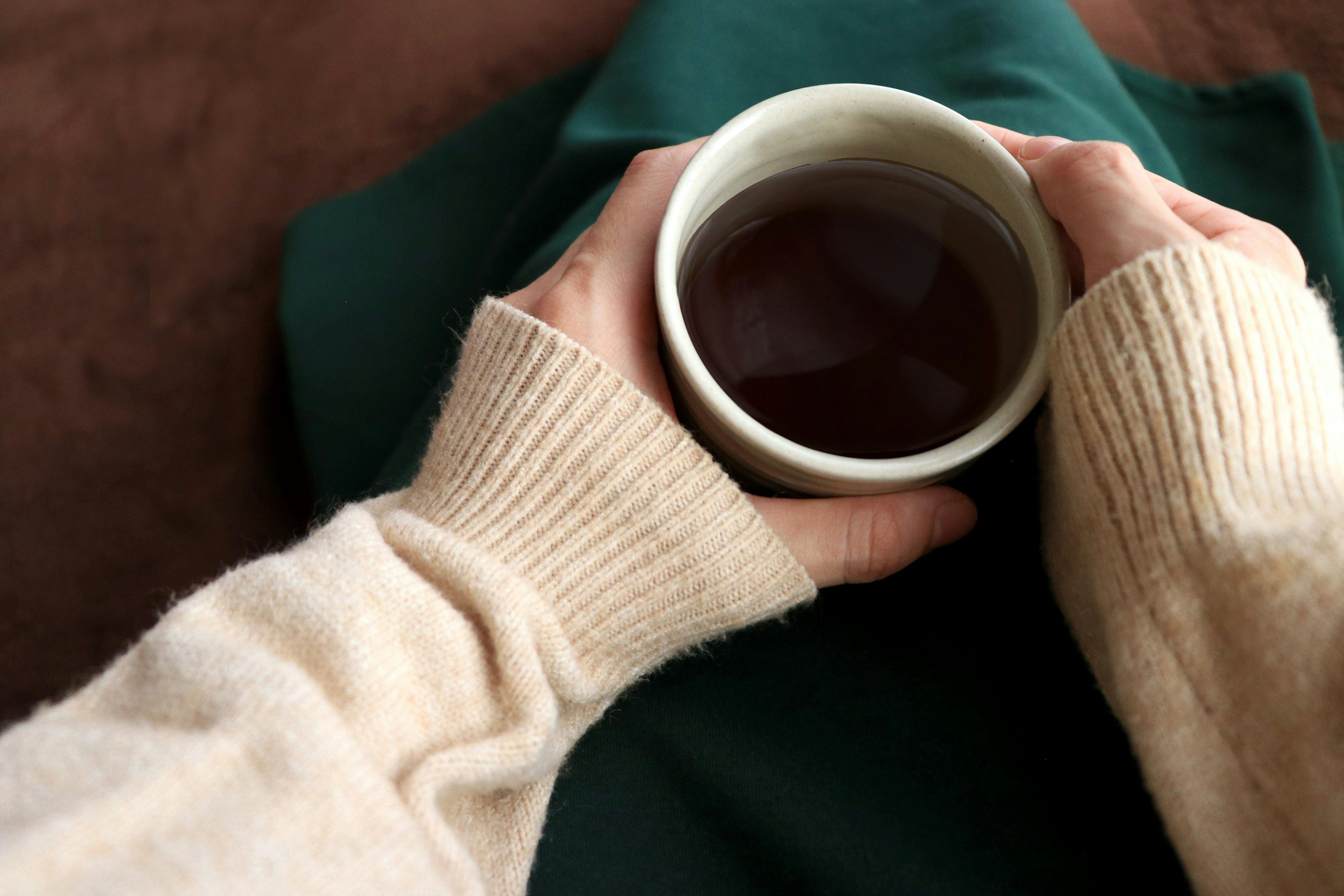 Hands holding a warm drink in a cozy sweater