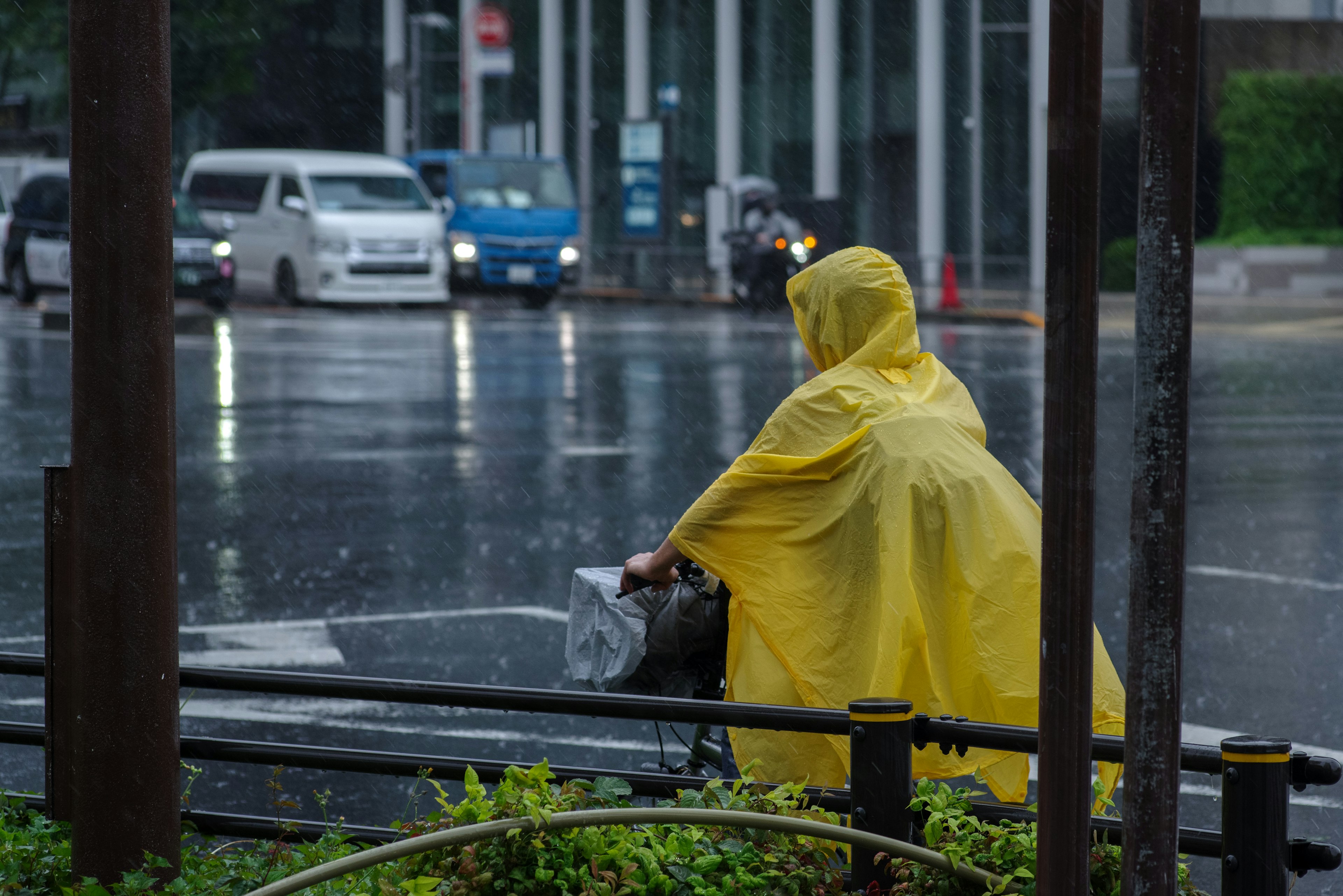 คนที่สวมเสื้อกันฝนสีเหลืองกำลังผลักจักรยานในสายฝน