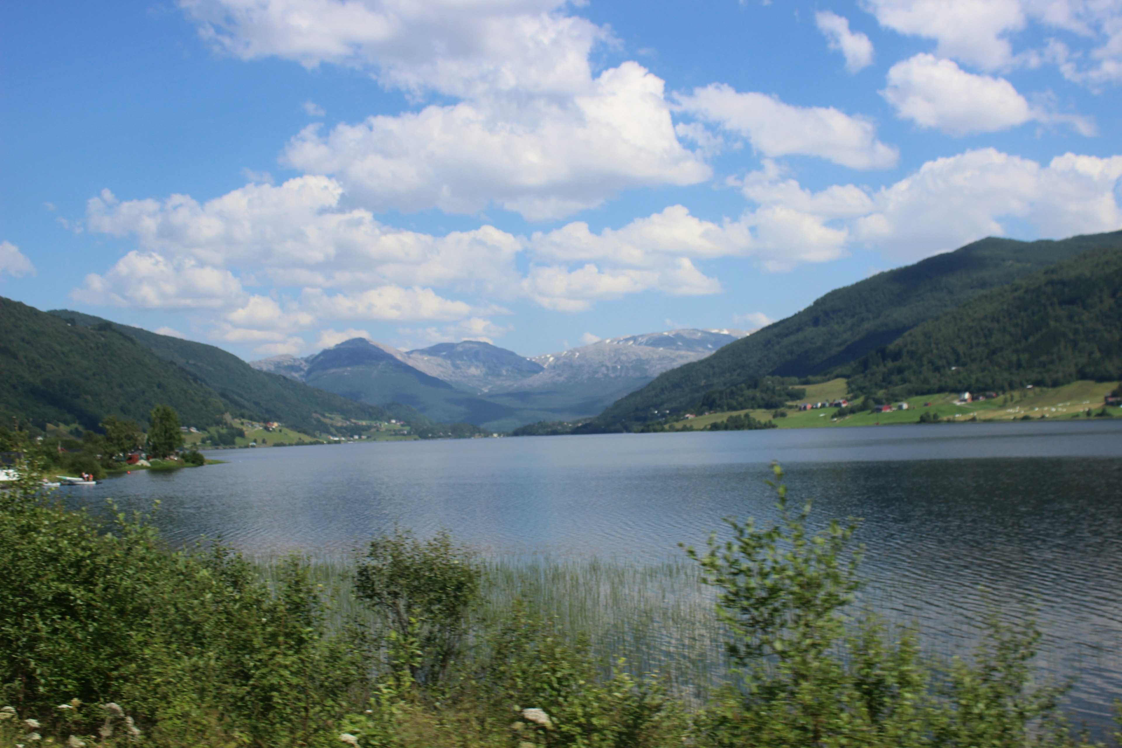 Vista escénica de un lago rodeado de montañas cielo azul y nubes esponjosas