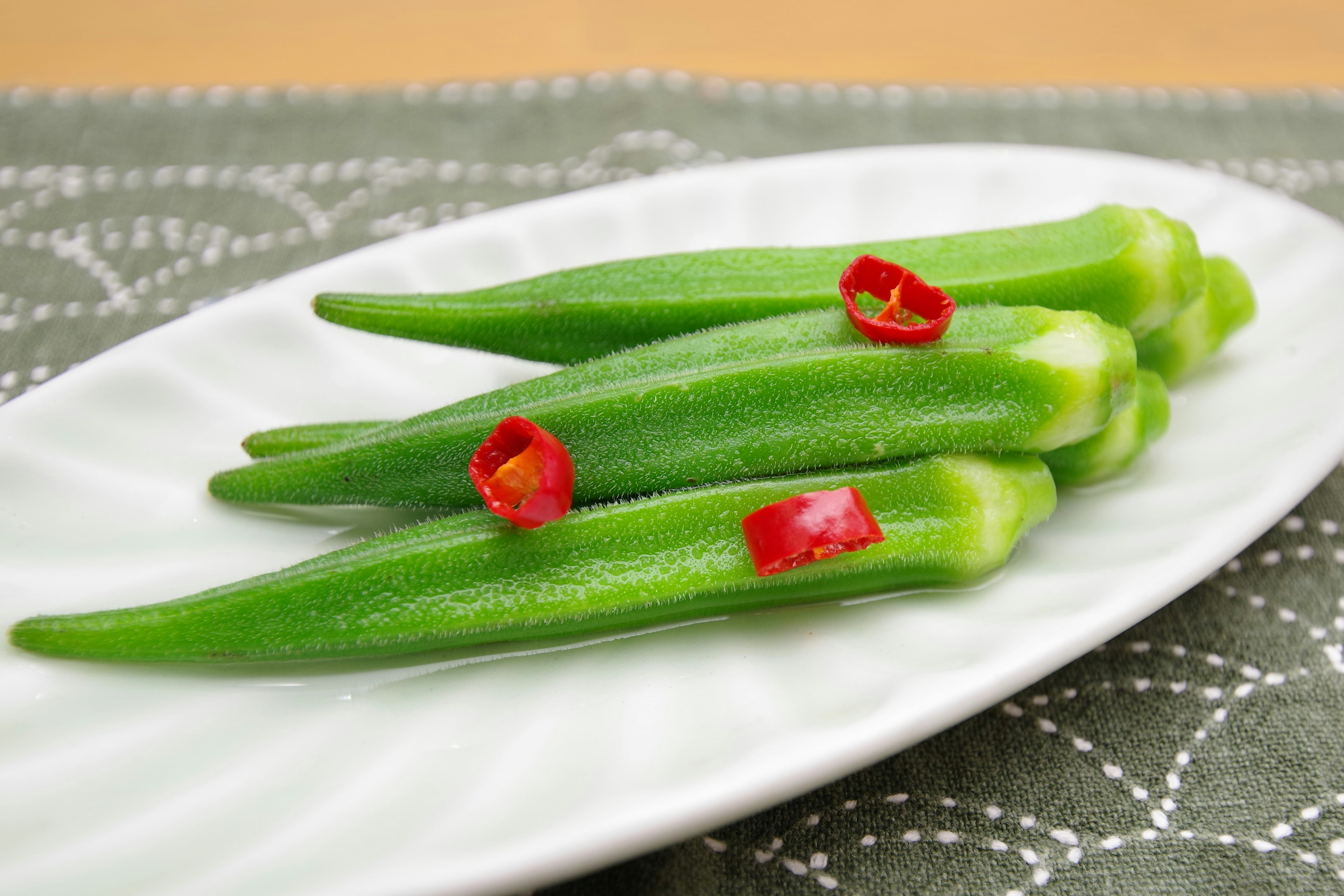 Fresh okra and sliced red chili peppers on a white plate