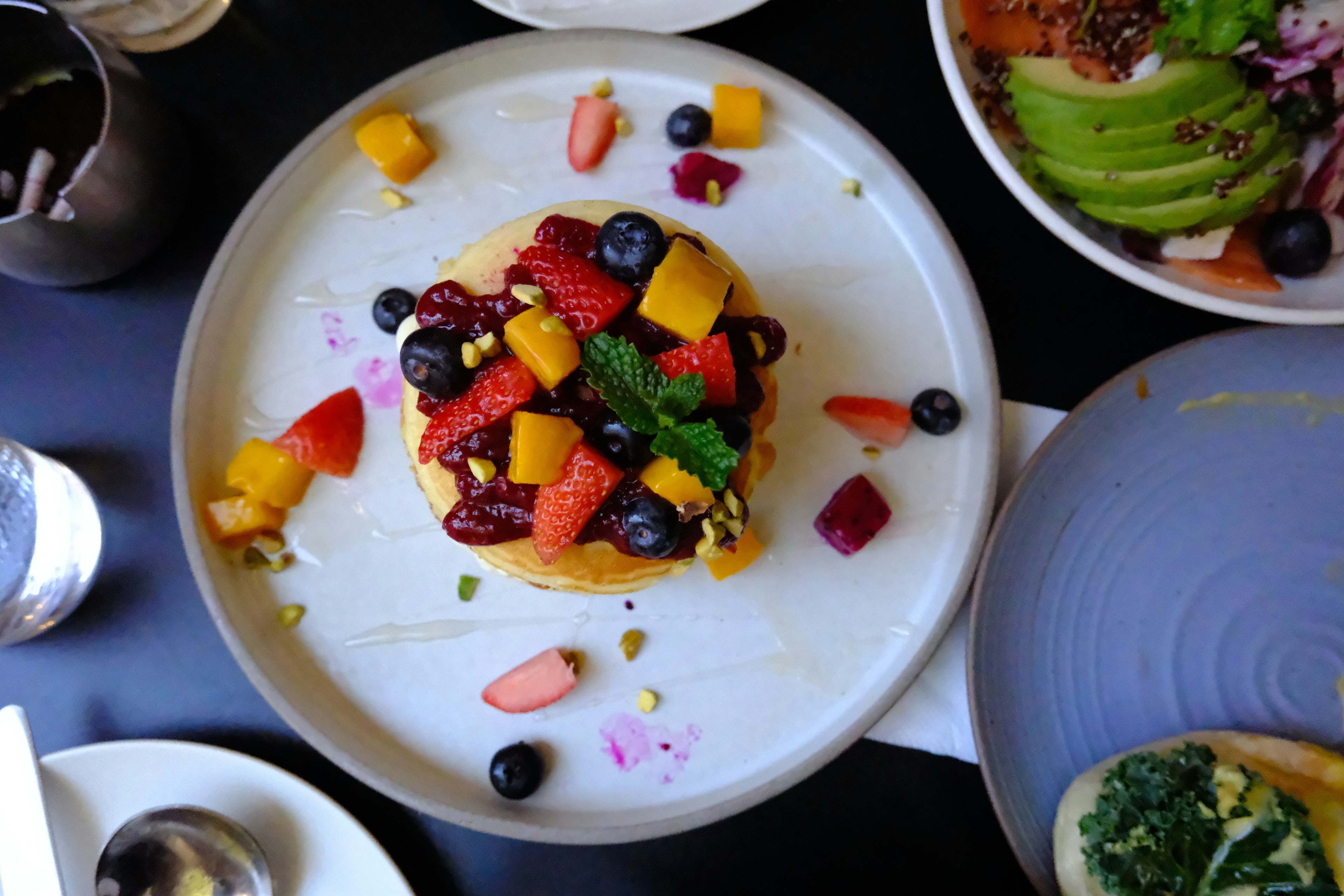 Colorful fruit-topped pancake in the center with other dishes visible around