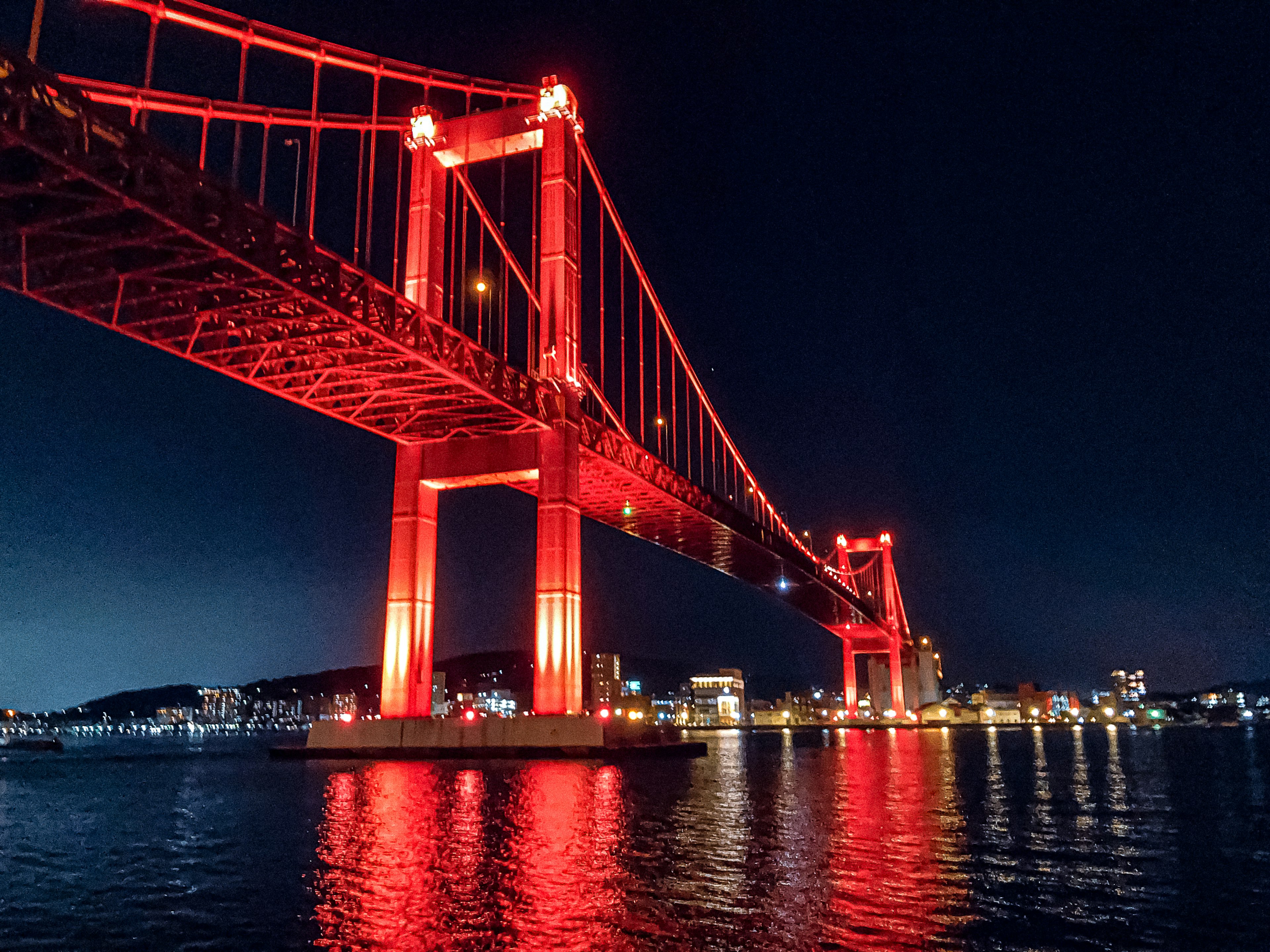 Brücke bei Nacht mit roten Lichtern beleuchtet und Reflexionen im Wasser