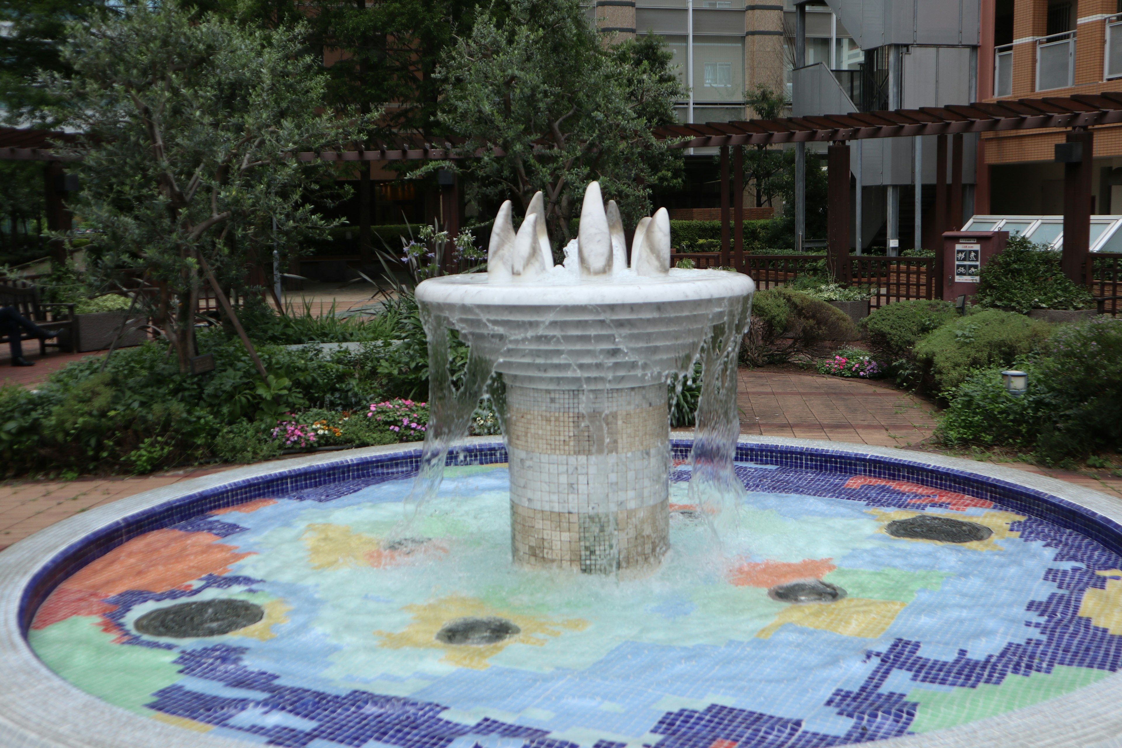 A beautiful garden scene featuring a water fountain surrounded by lush greenery and colorful tiled basin