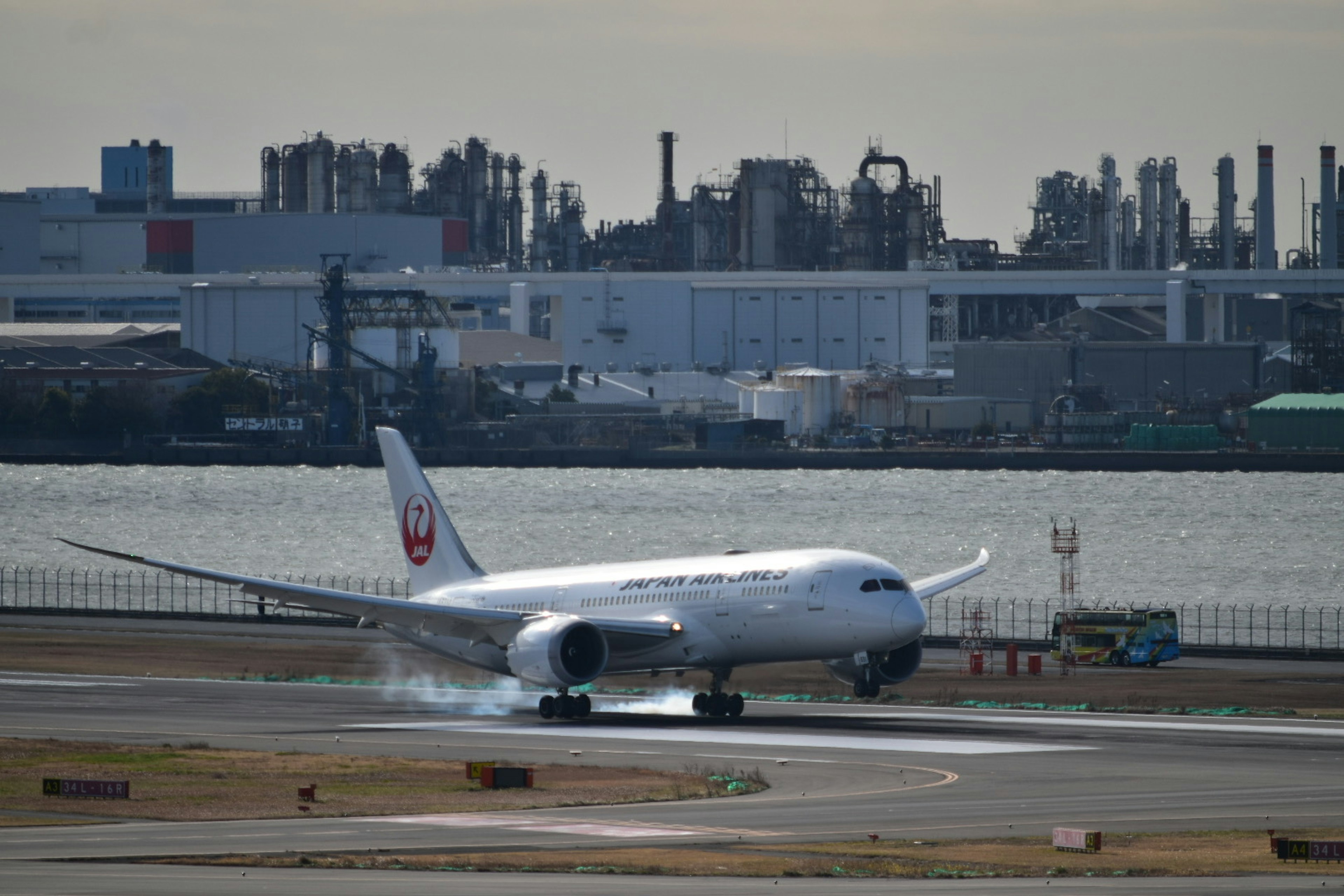 日本航空波音787在跑道上滑行，背景是工业区