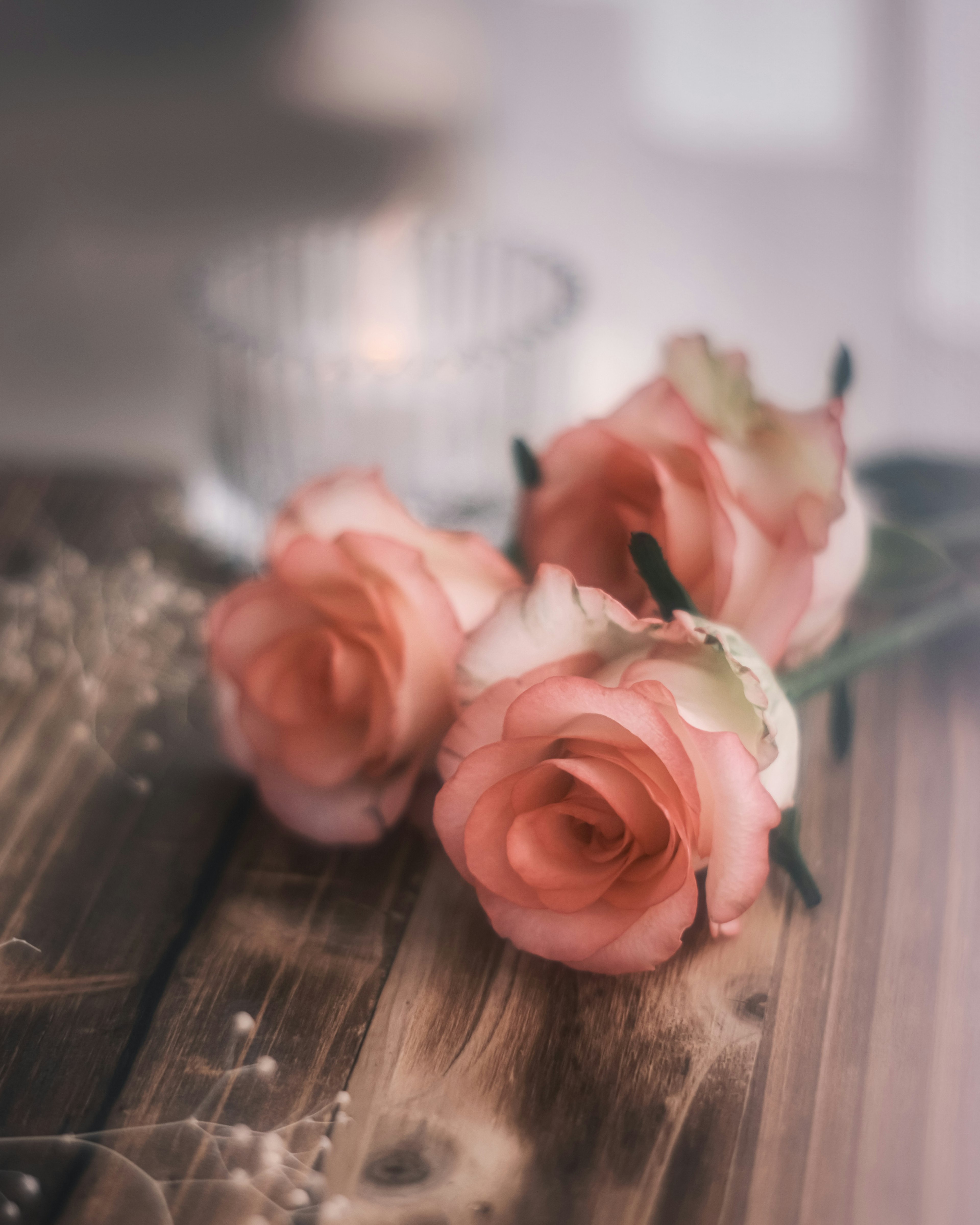 Three soft pink roses resting on a wooden table with a candle in the background