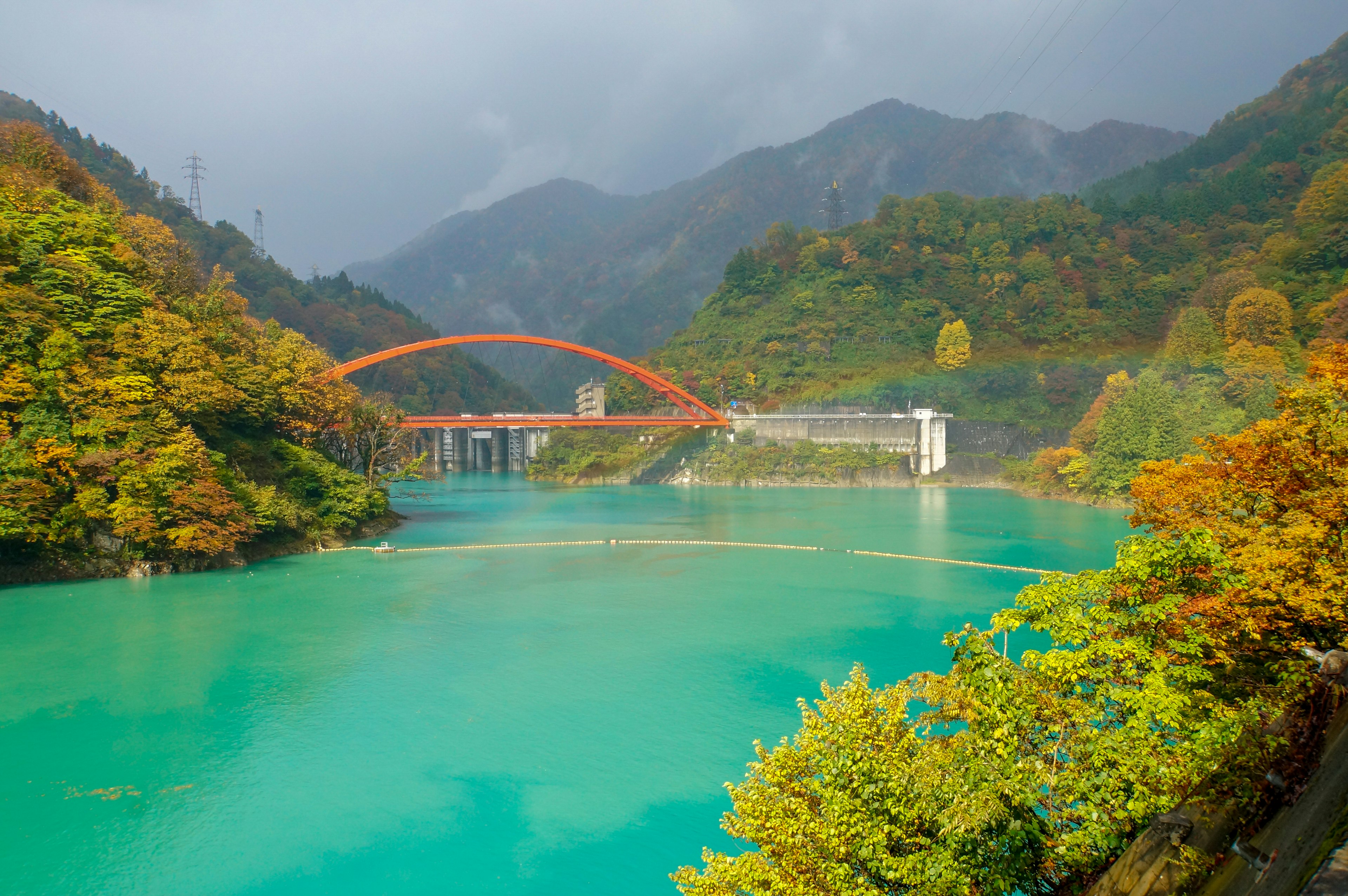 ทะเลสาบสีฟ้าอมเขียวที่สวยงามล้อมรอบด้วยภูเขาสีฤดูใบไม้ร่วงพร้อมสะพานโค้งสีแดง