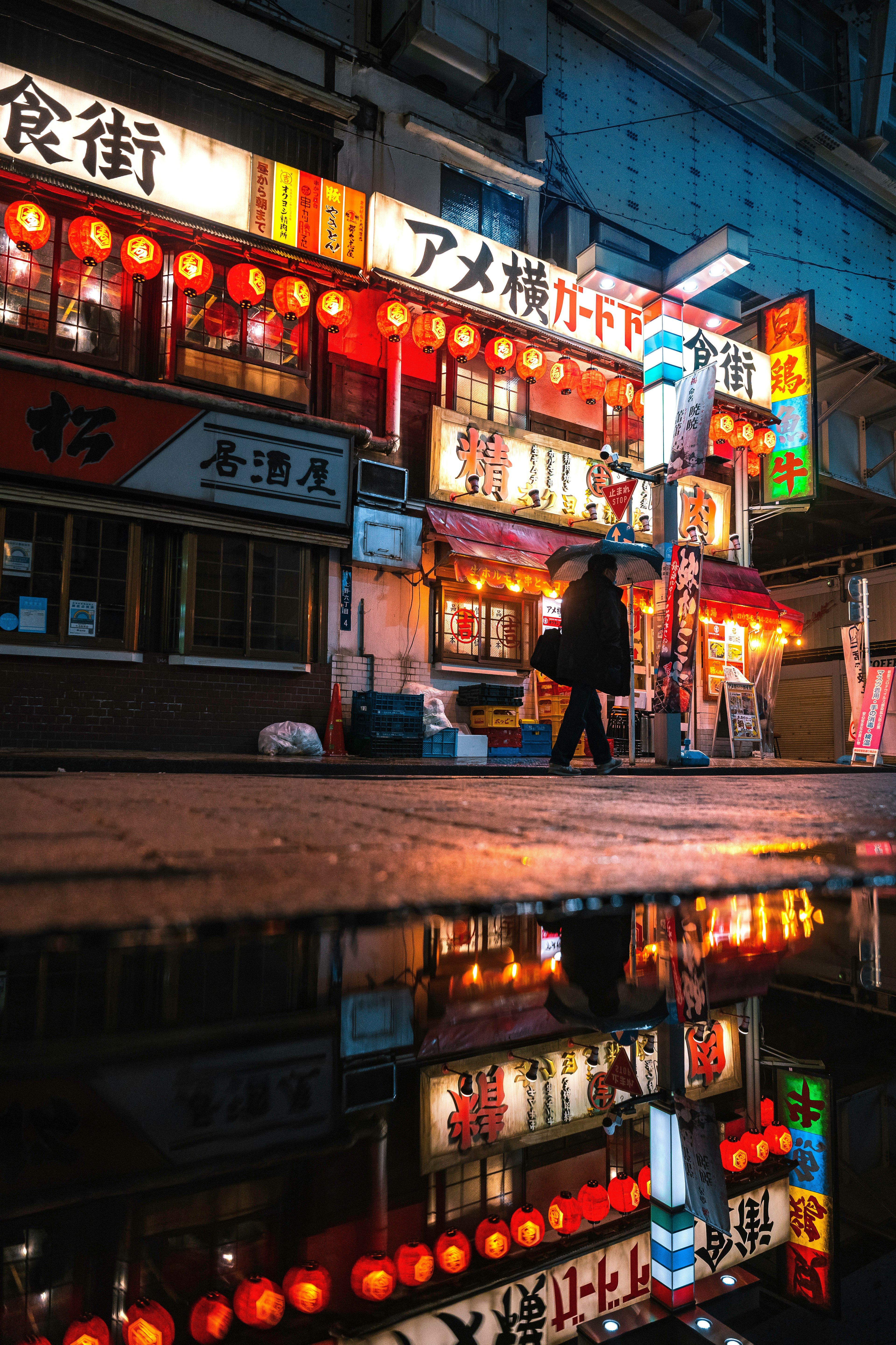 雨に濡れた街角でのネオン看板と提灯の反射が印象的な風景