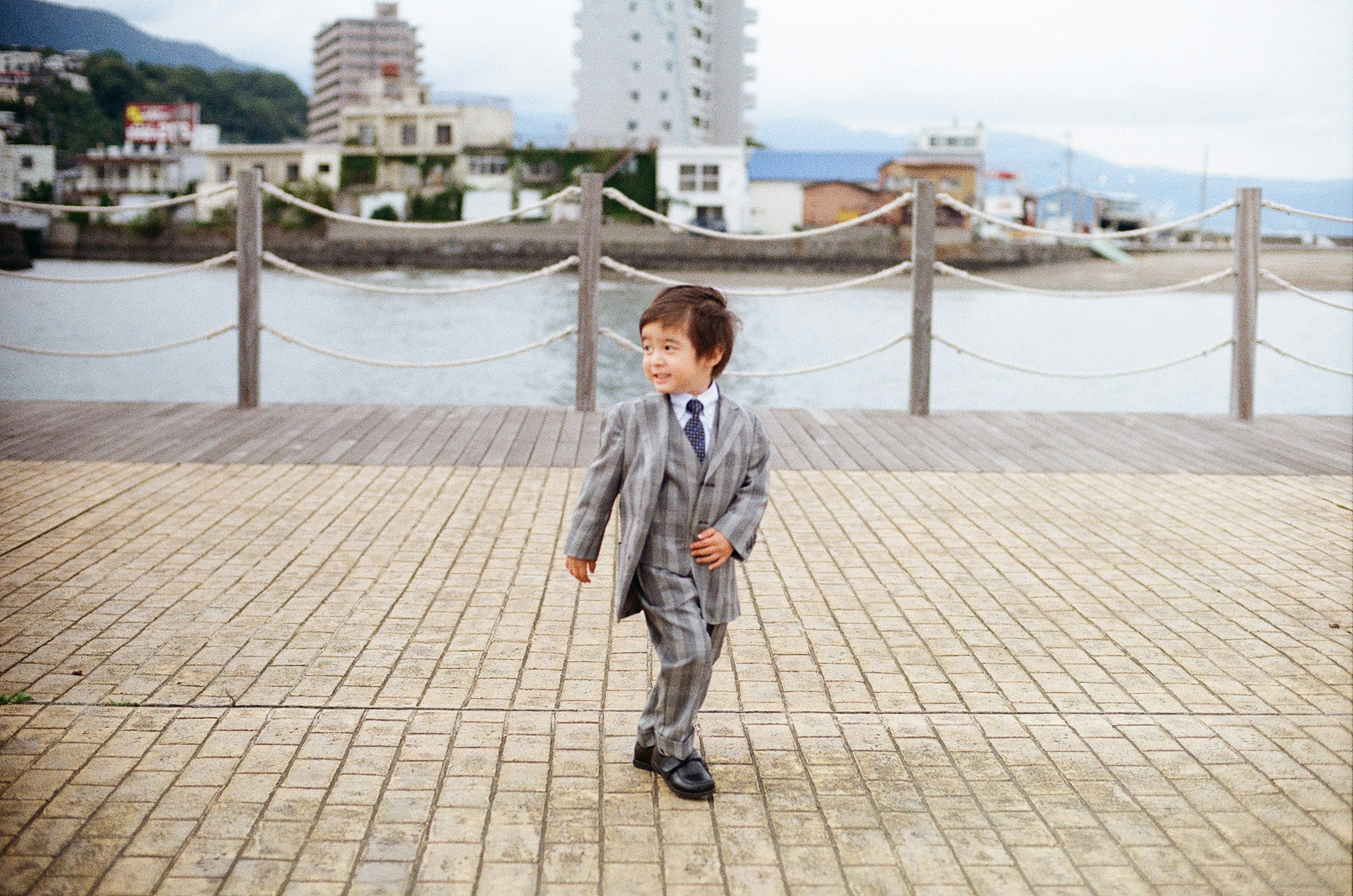 スーツを着た少年が海辺の遊歩道を歩いている