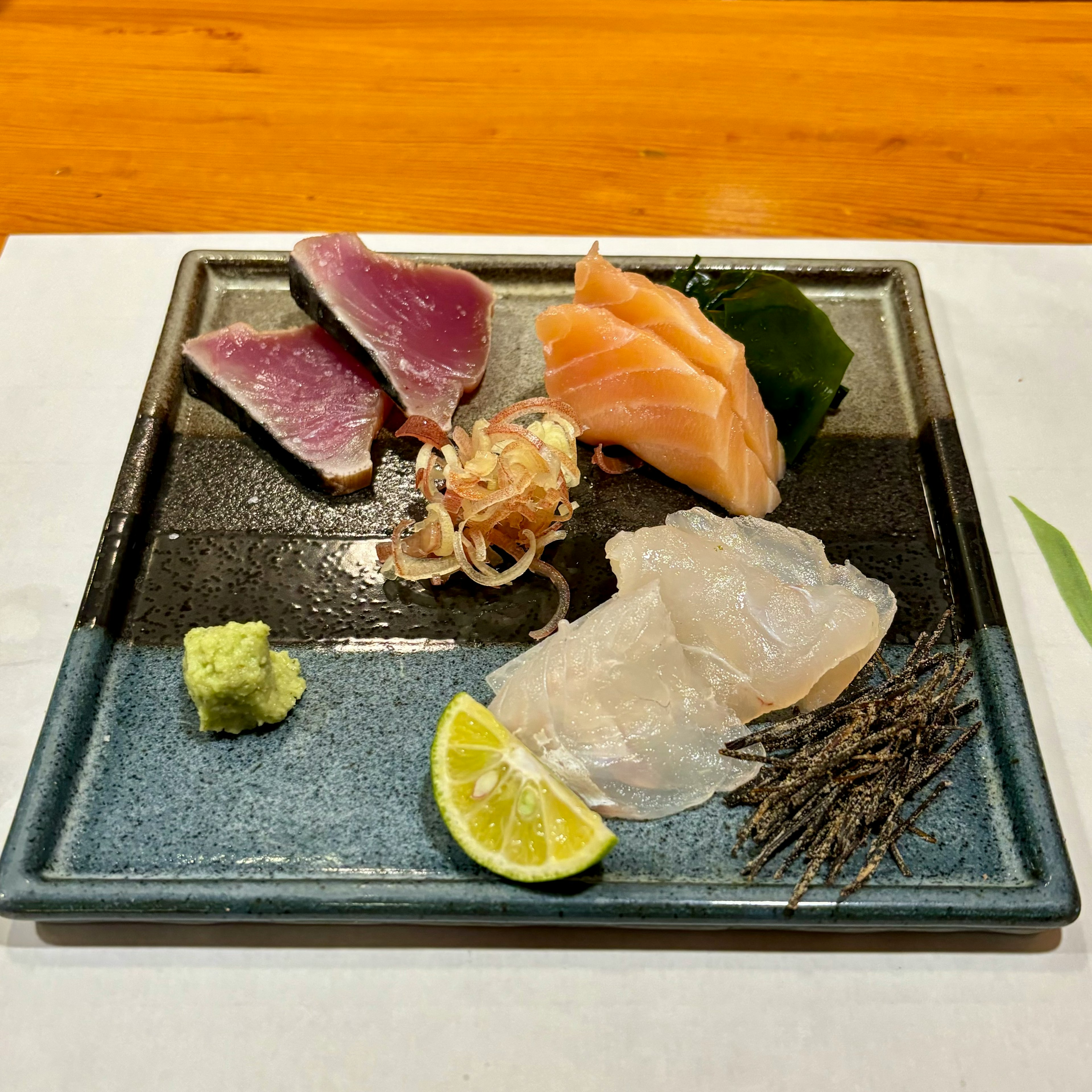 Piring sashimi segar dengan salmon, tuna, dan ikan putih dihias dengan jeruk nipis dan wasabi