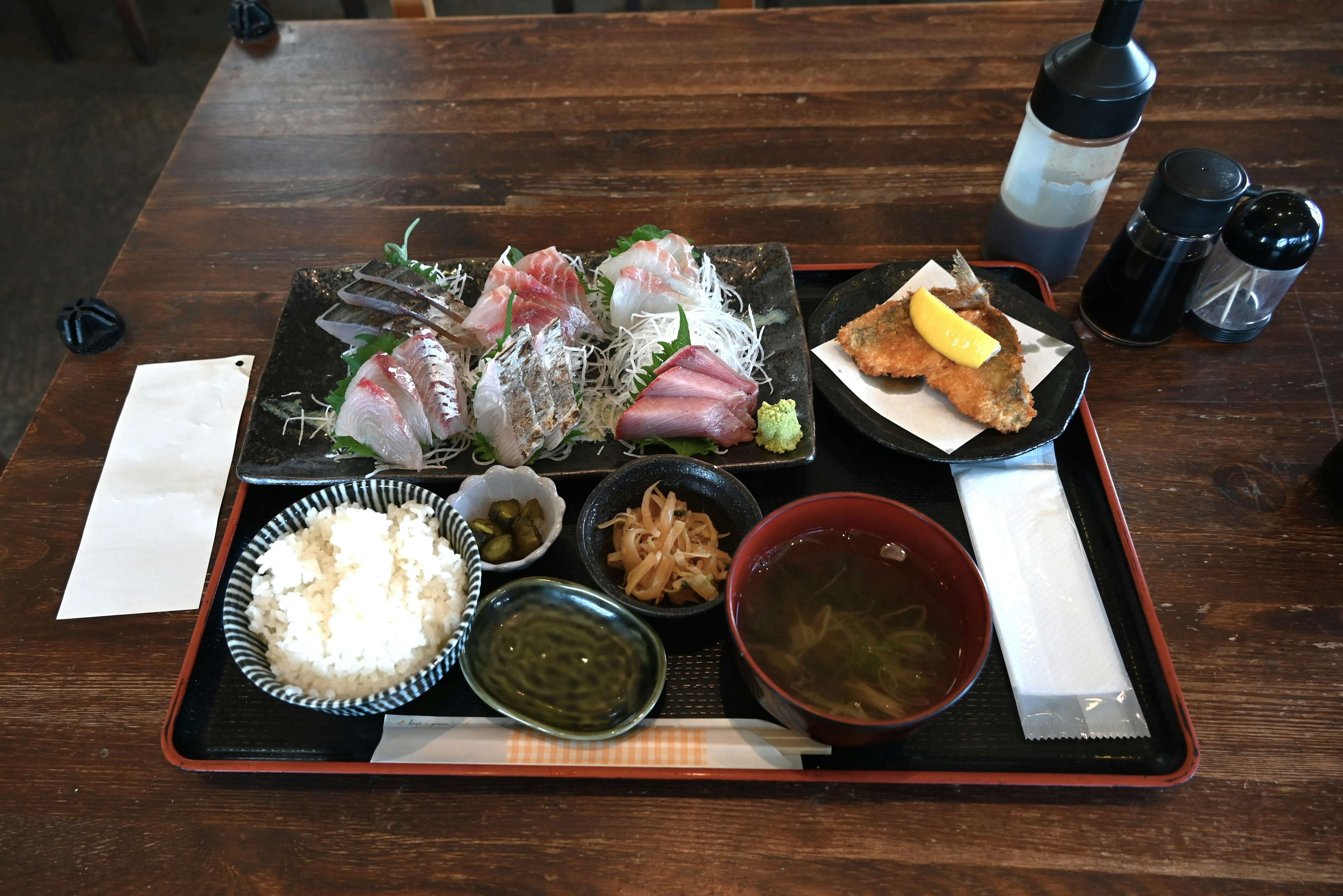 A Japanese meal featuring fresh sashimi with rice, miso soup, and pickles