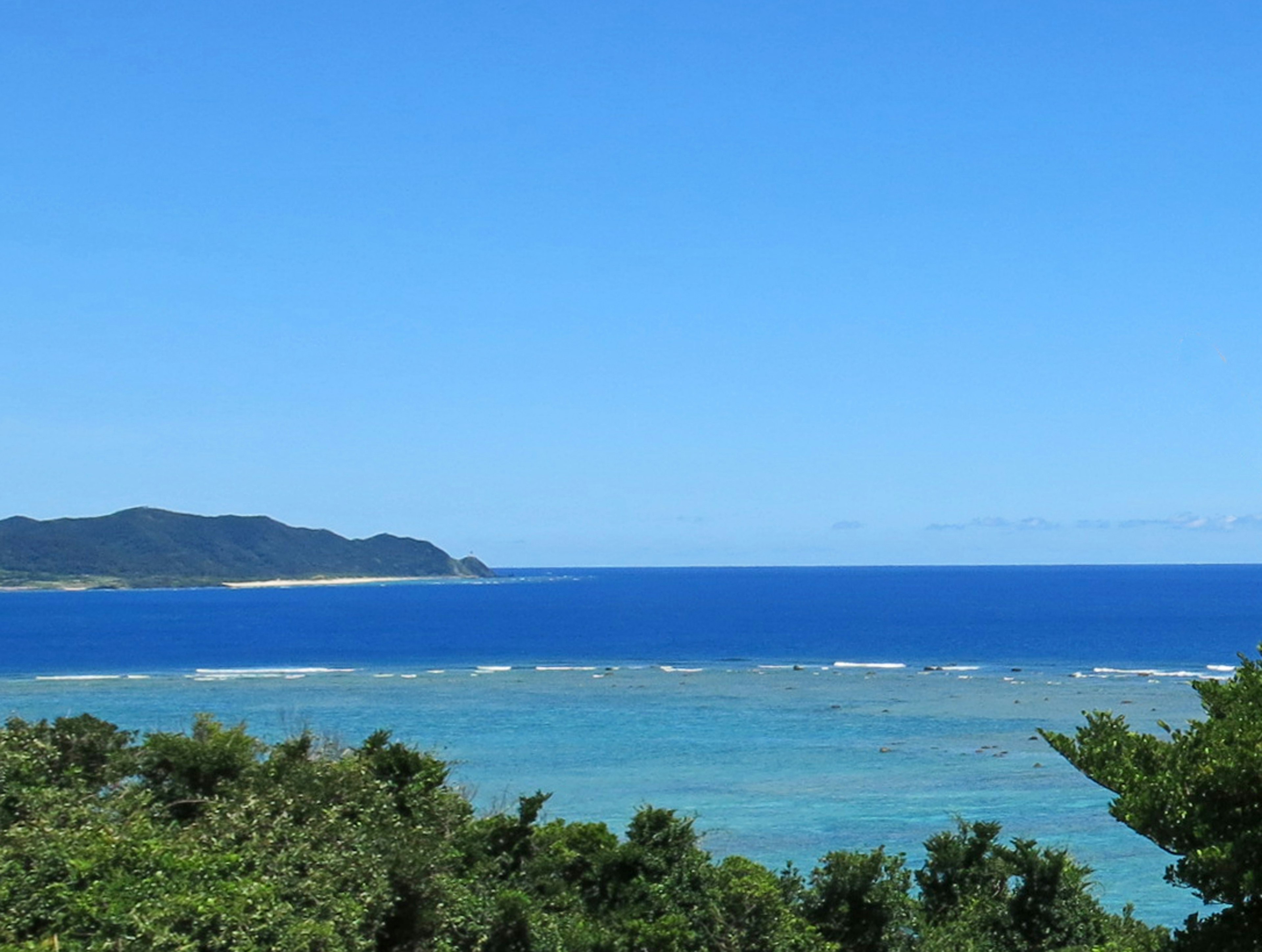 Beautiful landscape of blue sea and sky with visible island and coral reef