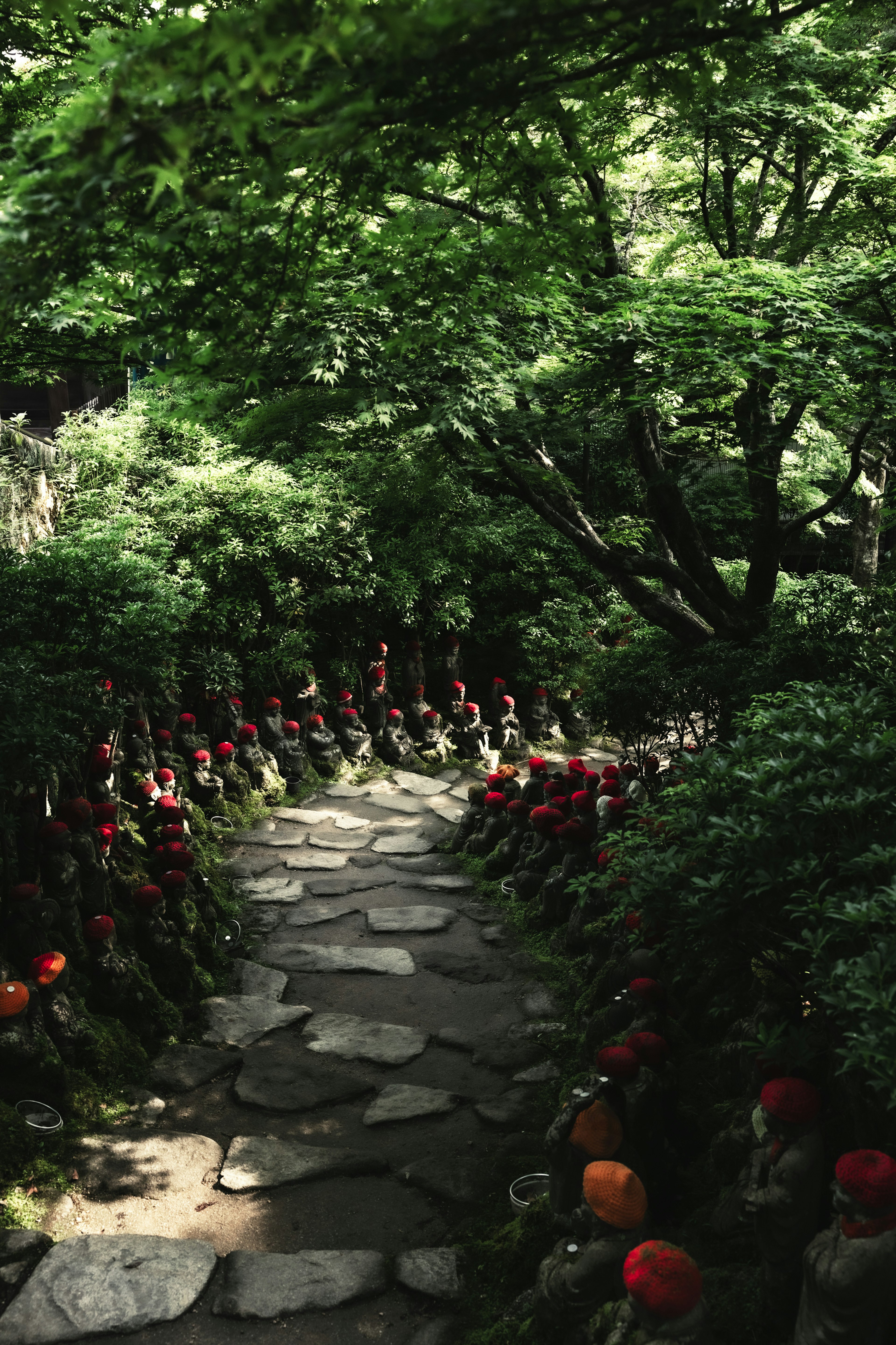 Camino de piedra flanqueado por pequeñas estatuas con sombreros rojos y árboles verdes exuberantes