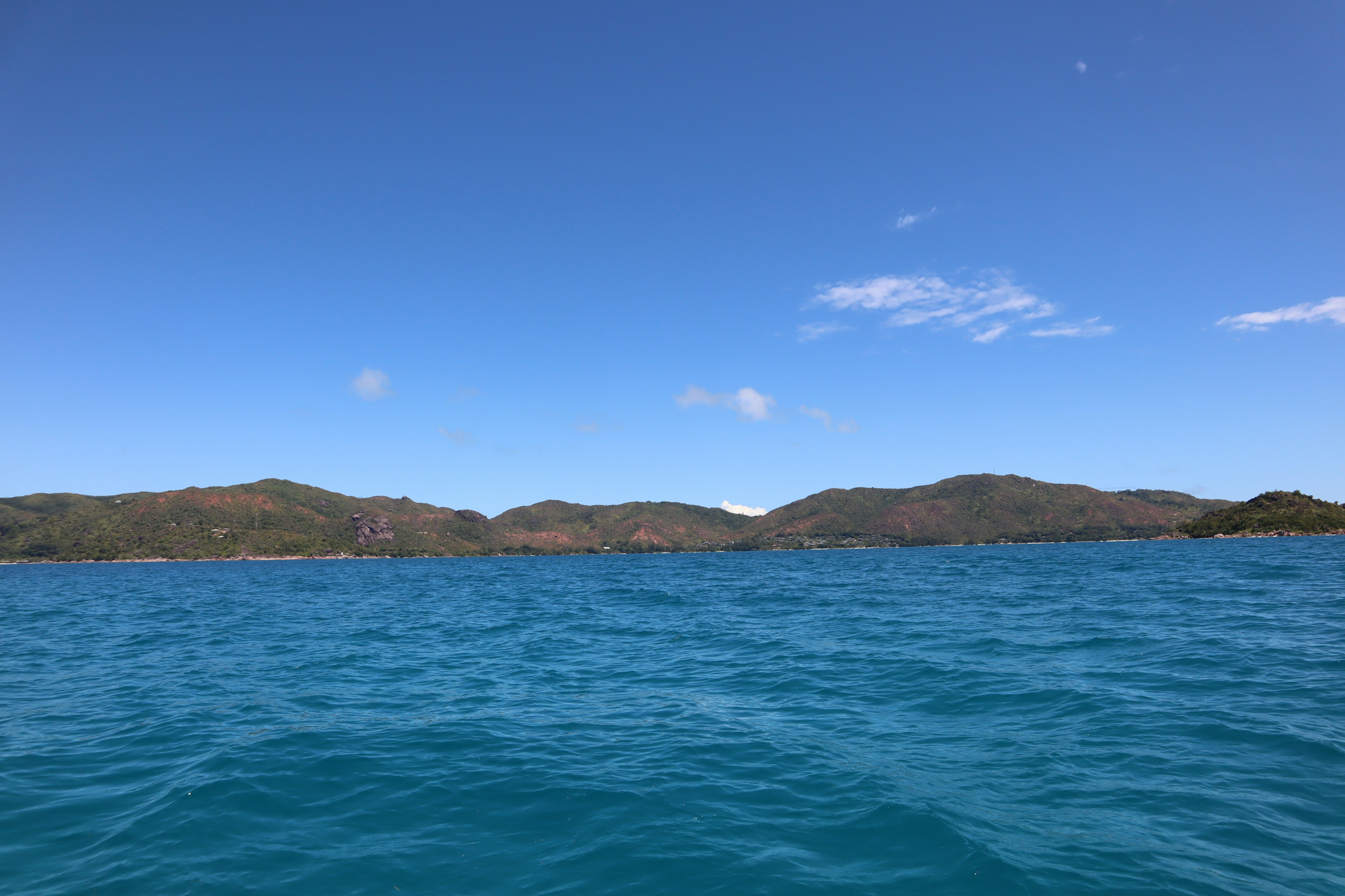 Pemandangan laut biru dan bukit hijau di bawah langit cerah