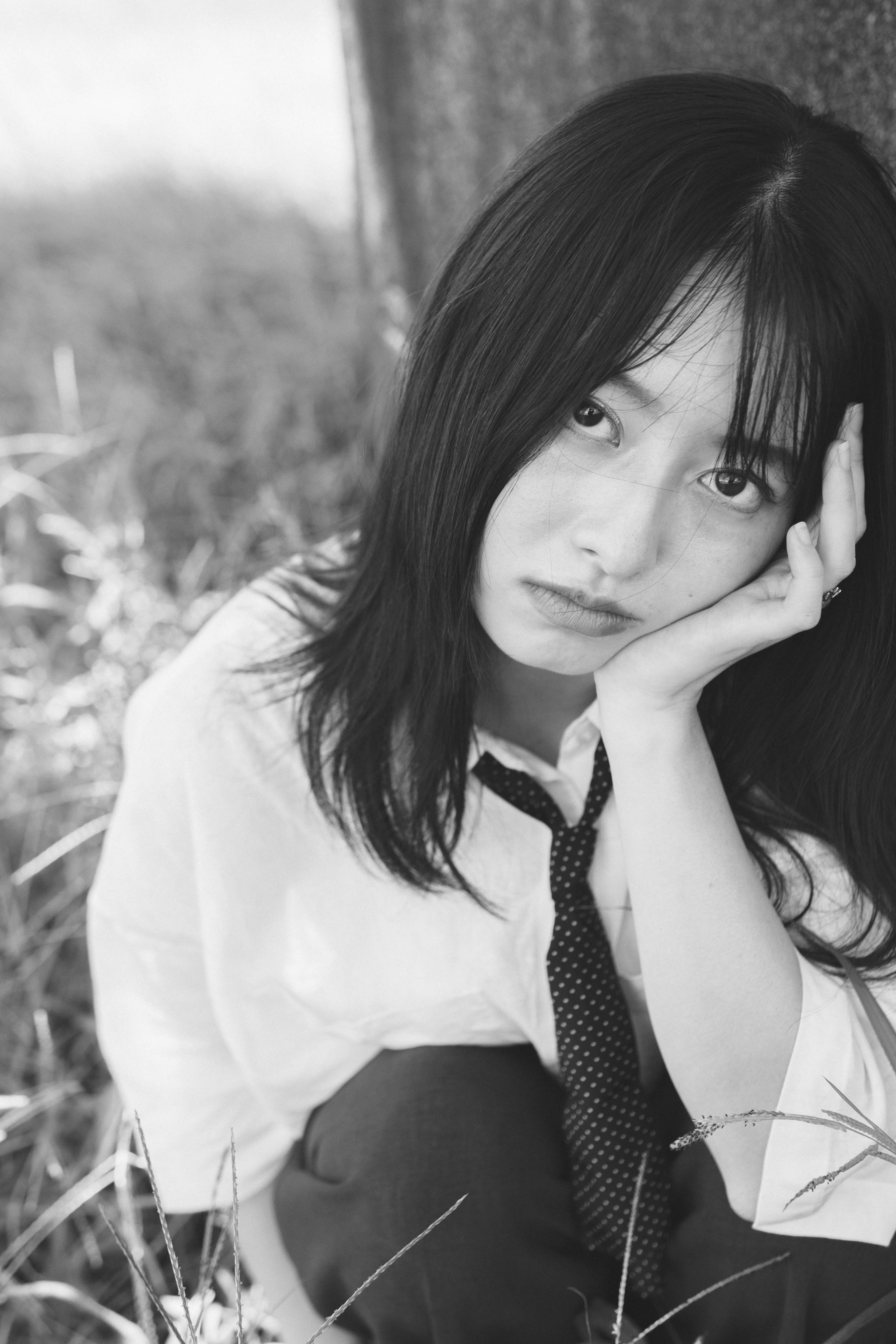 Black and white photo of a woman sitting on grass with a tired expression