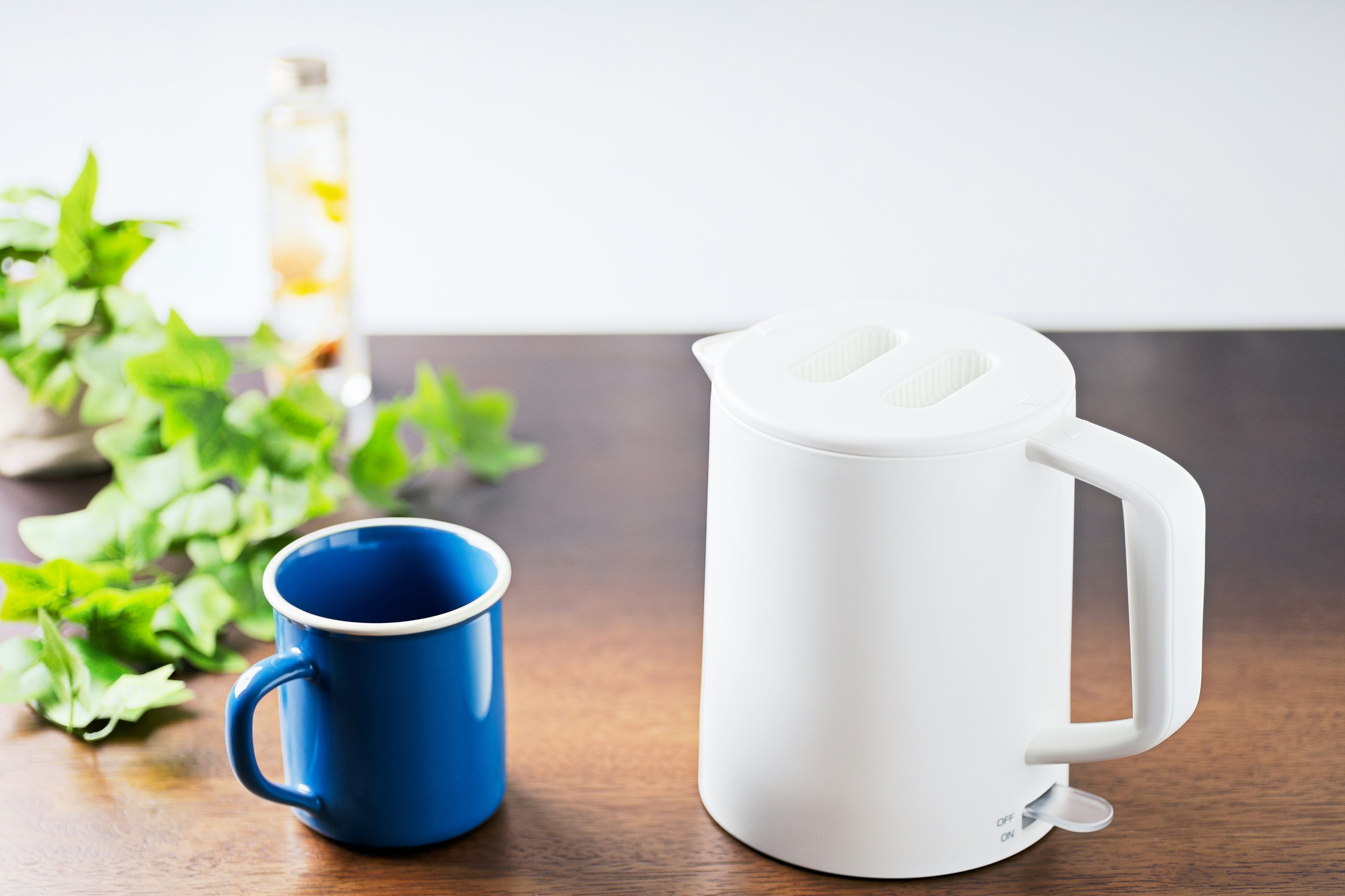 Una tetera eléctrica blanca y una taza azul sobre una mesa de madera