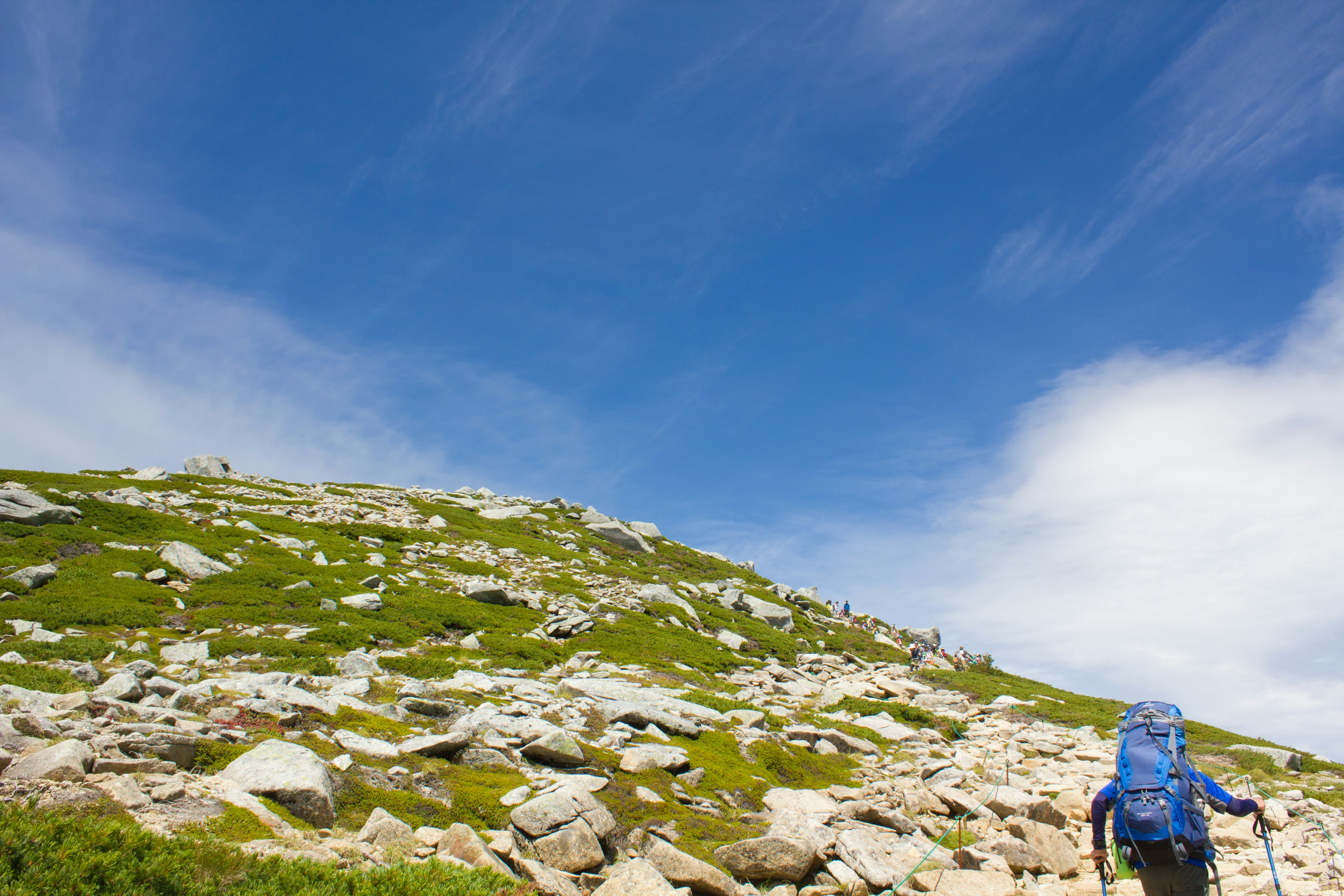 Escursionista con uno zaino grande che scala una collina rocciosa sotto un cielo blu