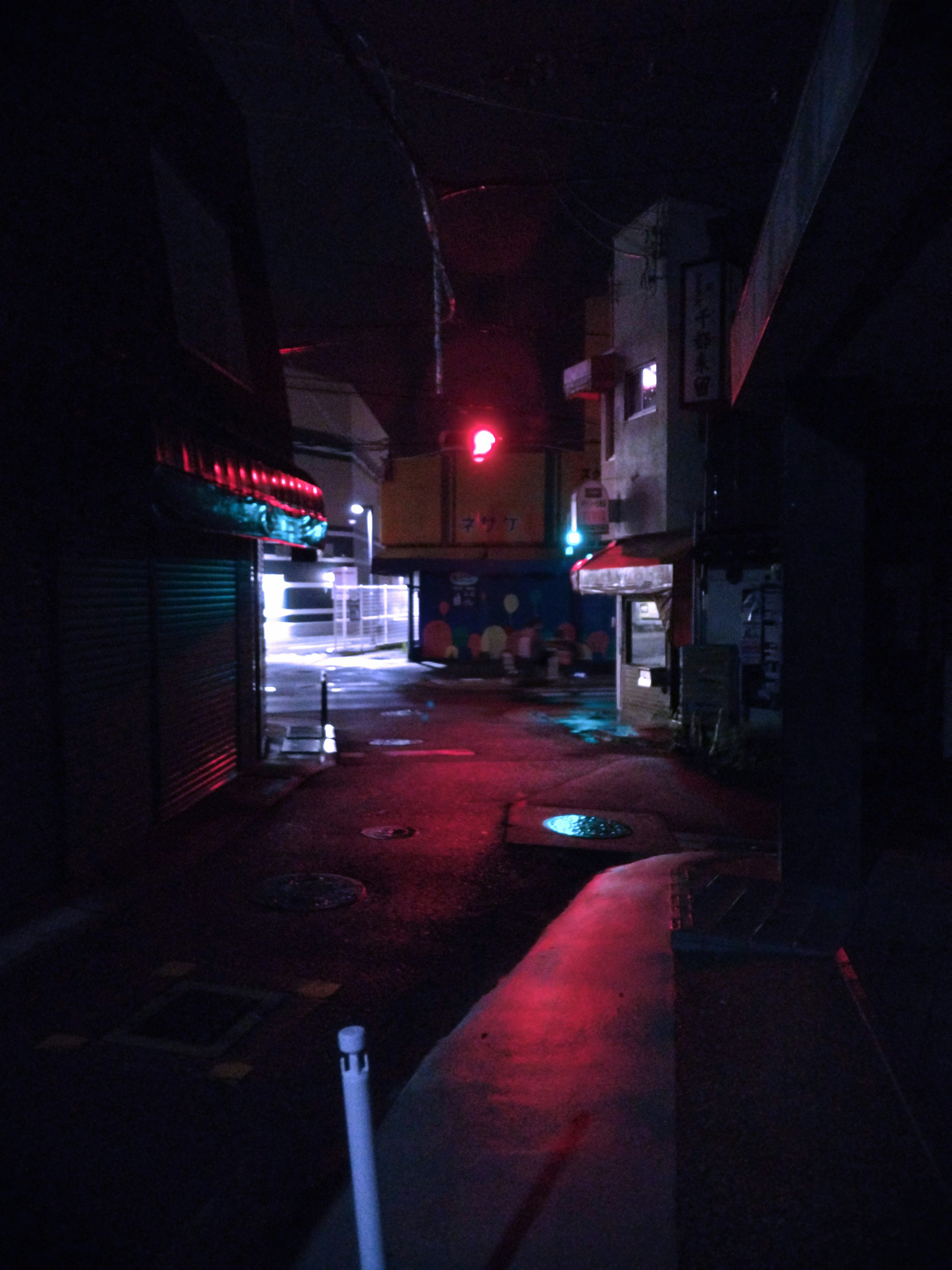 Night scene of a dark alley with a red traffic light and reflections of blue light