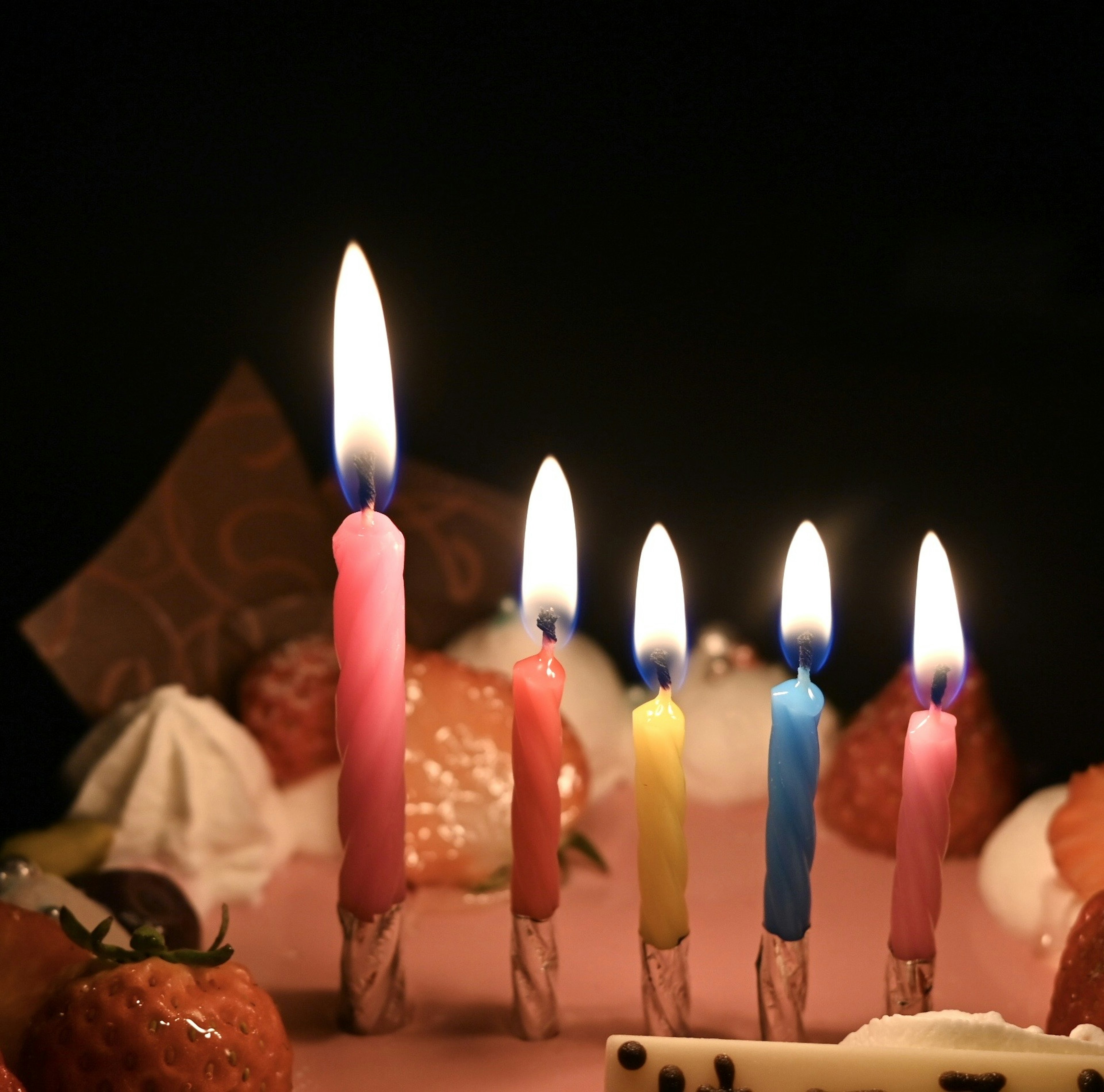 A close-up of a cake with lit colorful candles and various sweets