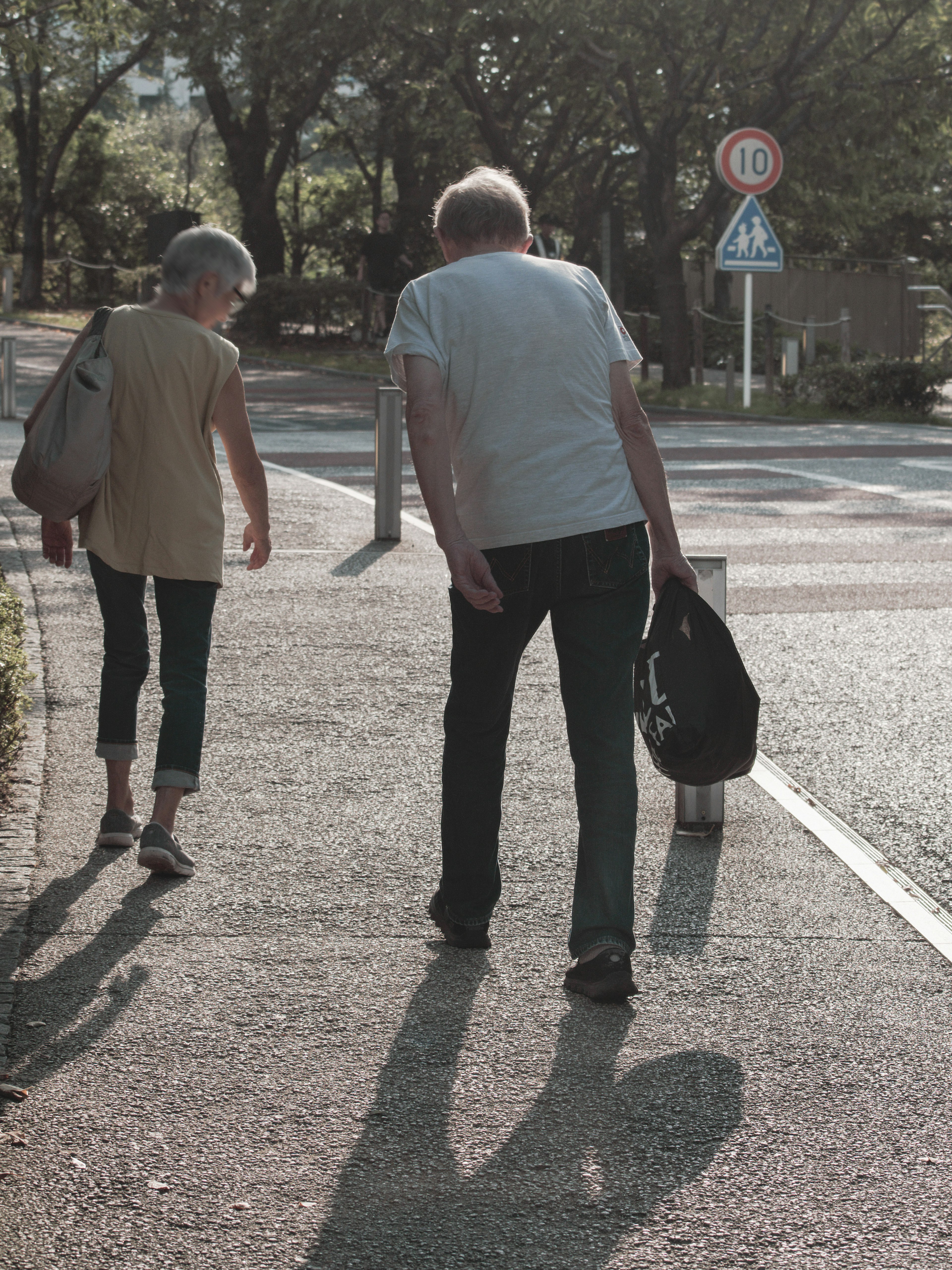 Dos personas mayores caminando por una acera de espaldas con sombras largas bajo la suave luz del sol