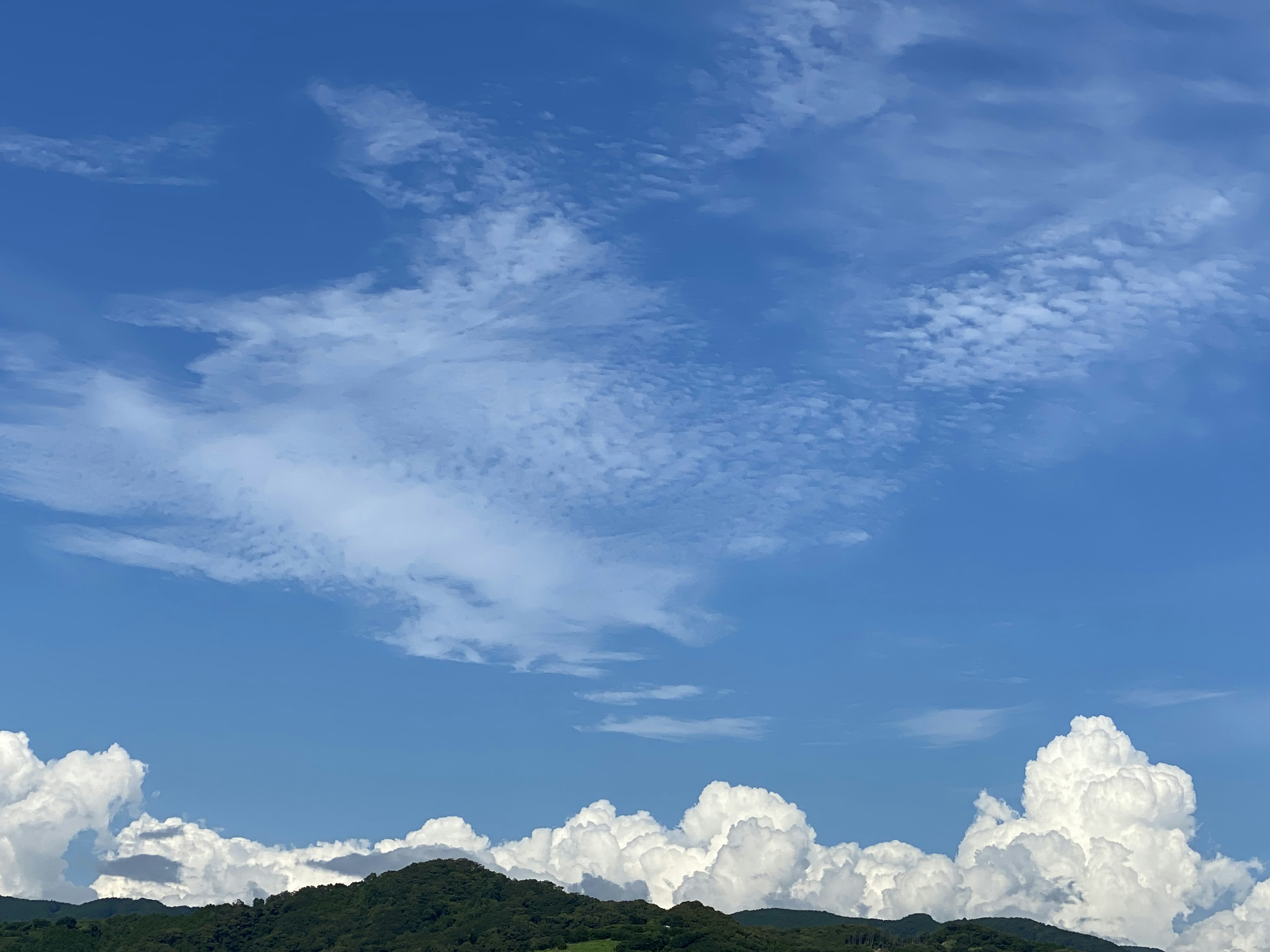 Un cielo azul claro con nubes blancas y la silueta de una montaña