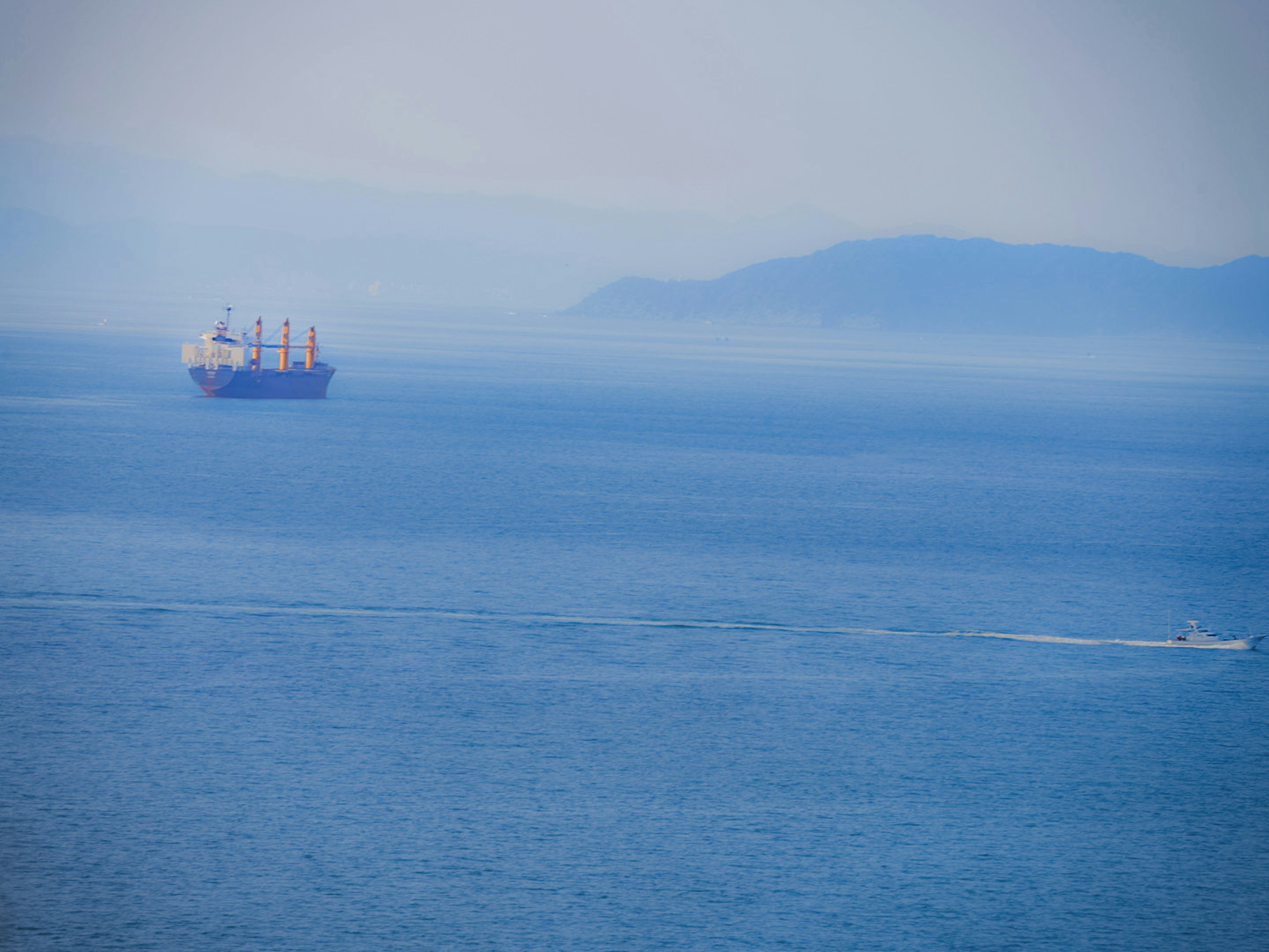 Cargo ship on blue sea with distant mountains