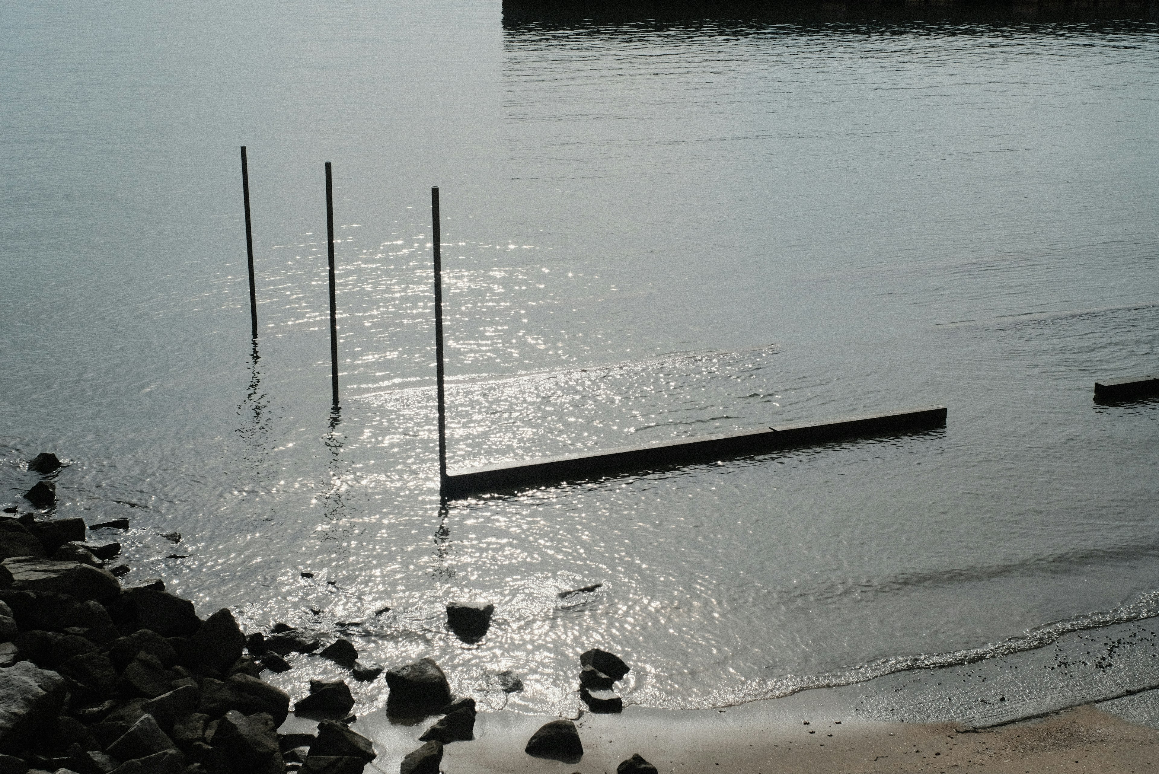 Ruhige Strandansicht mit Reflexionen auf dem Wasser und vertikalen Pfählen im Hintergrund