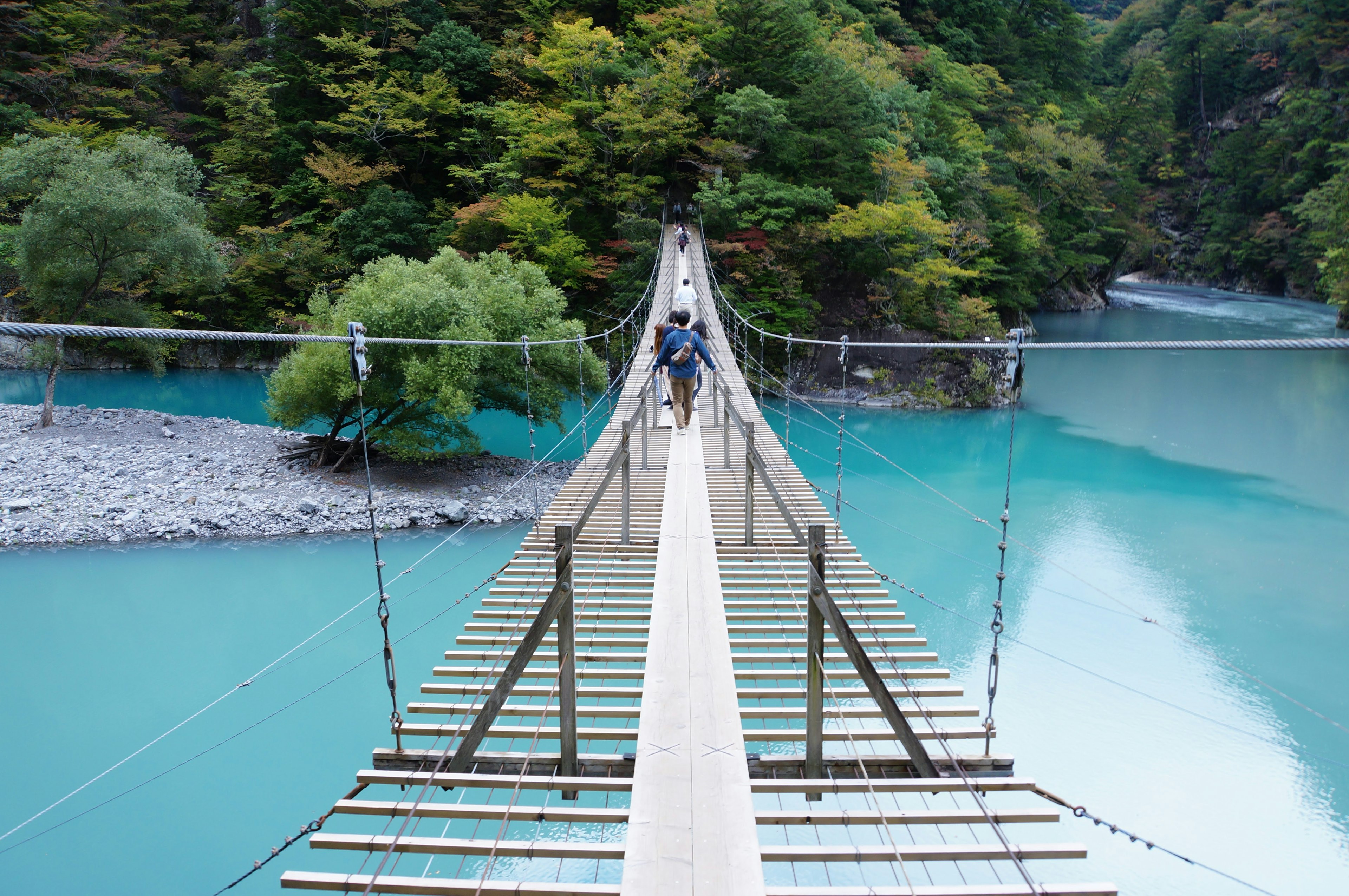 Suspension bridge over a turquoise river surrounded by lush greenery