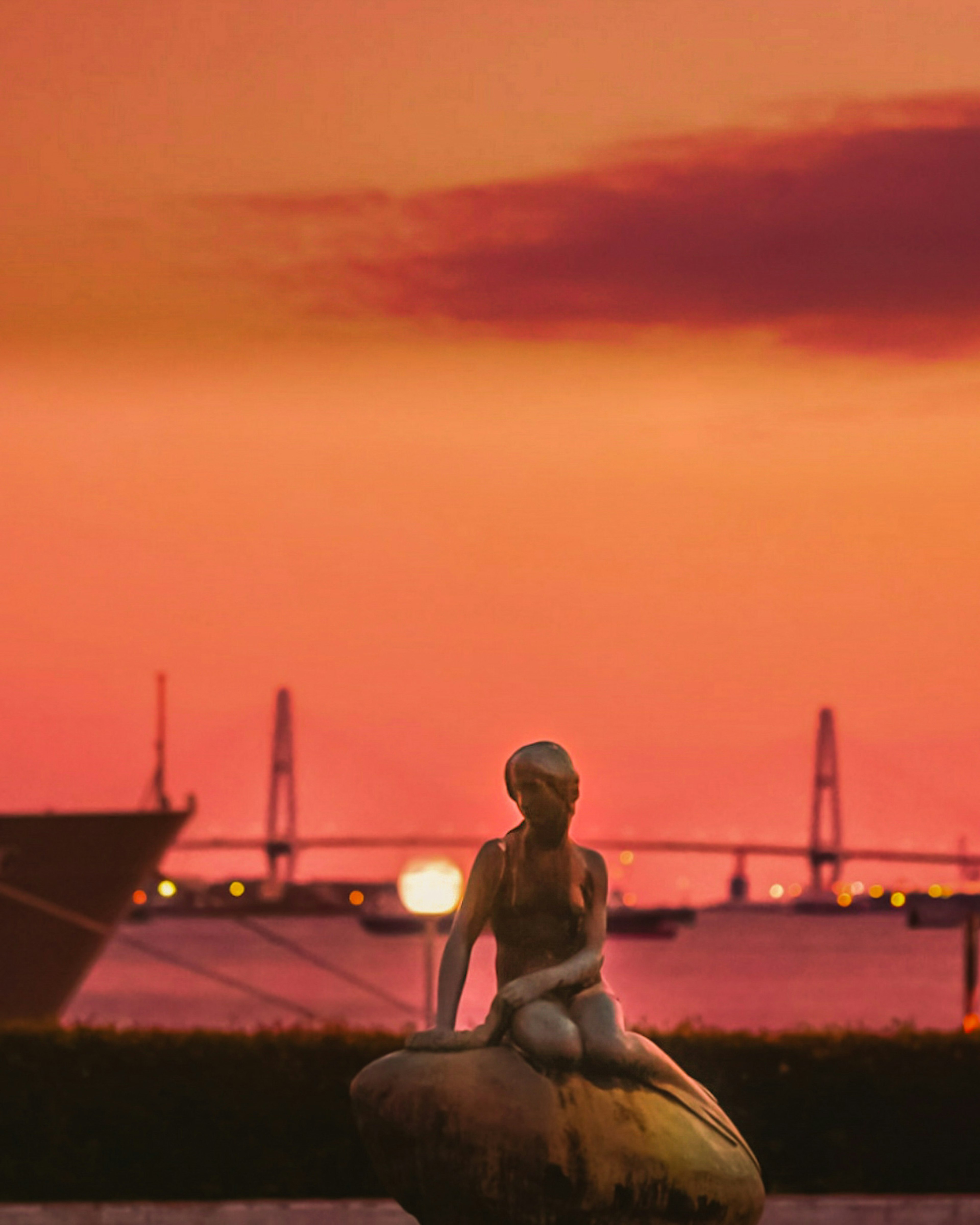 Mermaid statue sitting on a rock with sunset backdrop