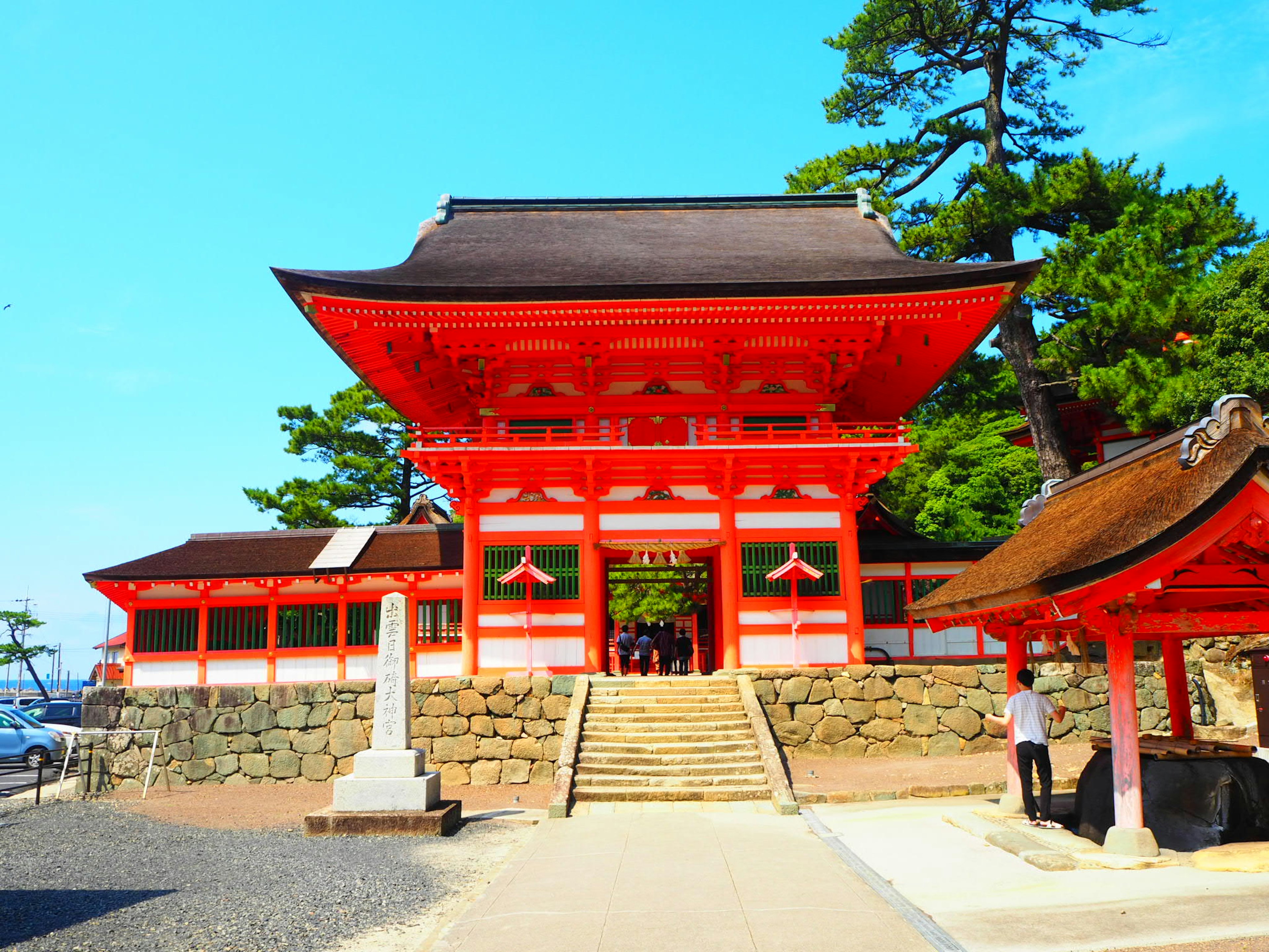 A vibrant red gate with a clear blue sky in the background showcasing a shrine