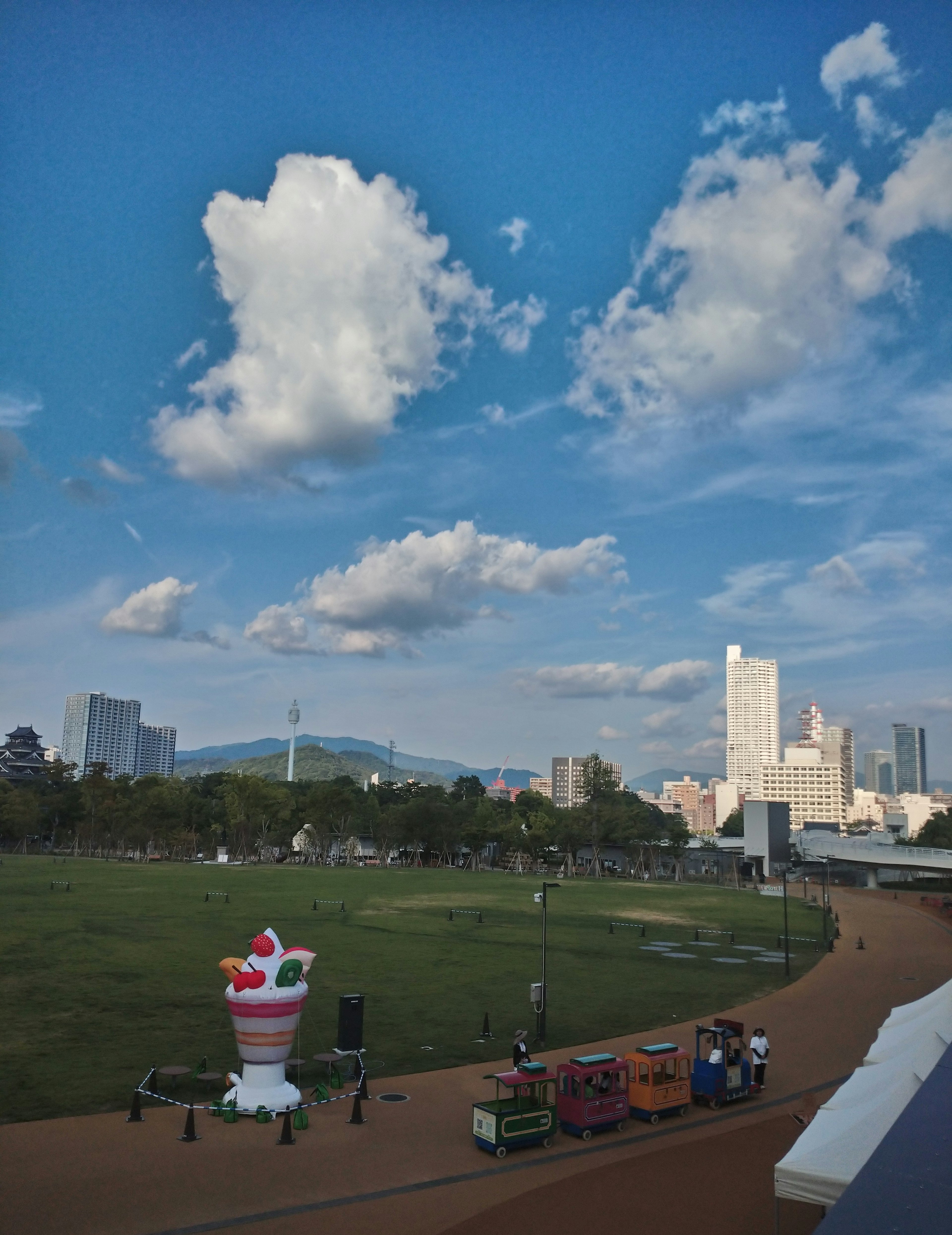 Una escena de parque con una gran escultura de helado y camiones de comida bajo un cielo azul