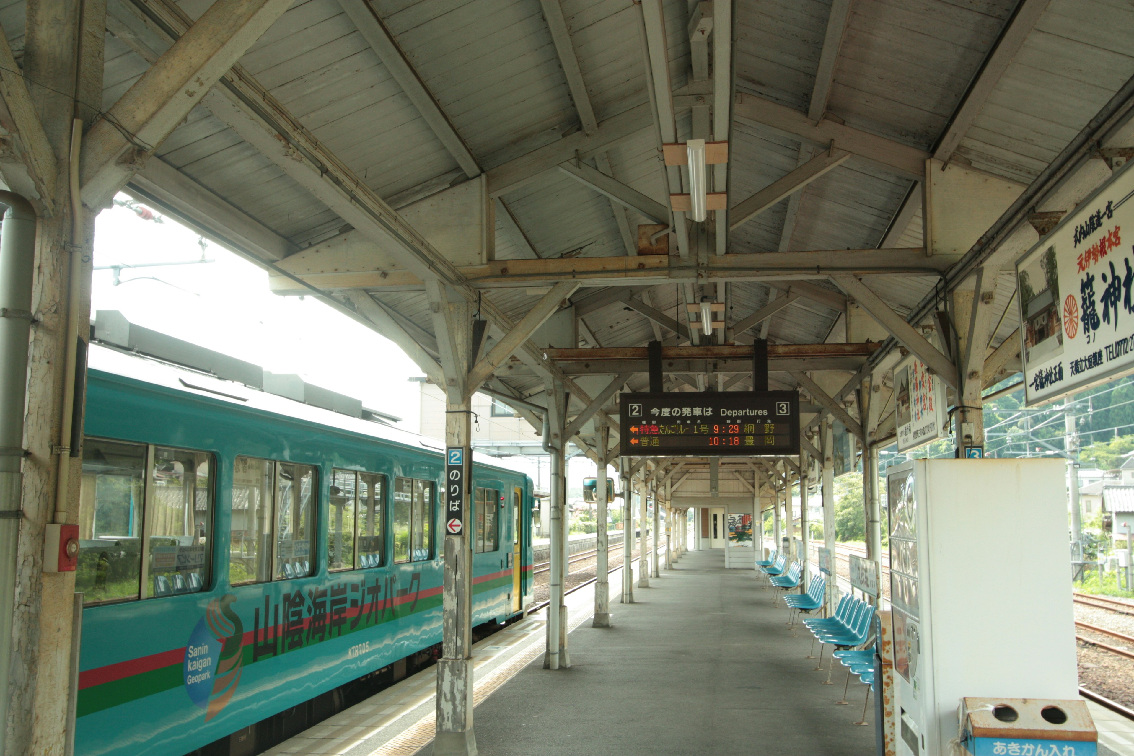 Plataforma con un tren azul y un tablero de horarios digital