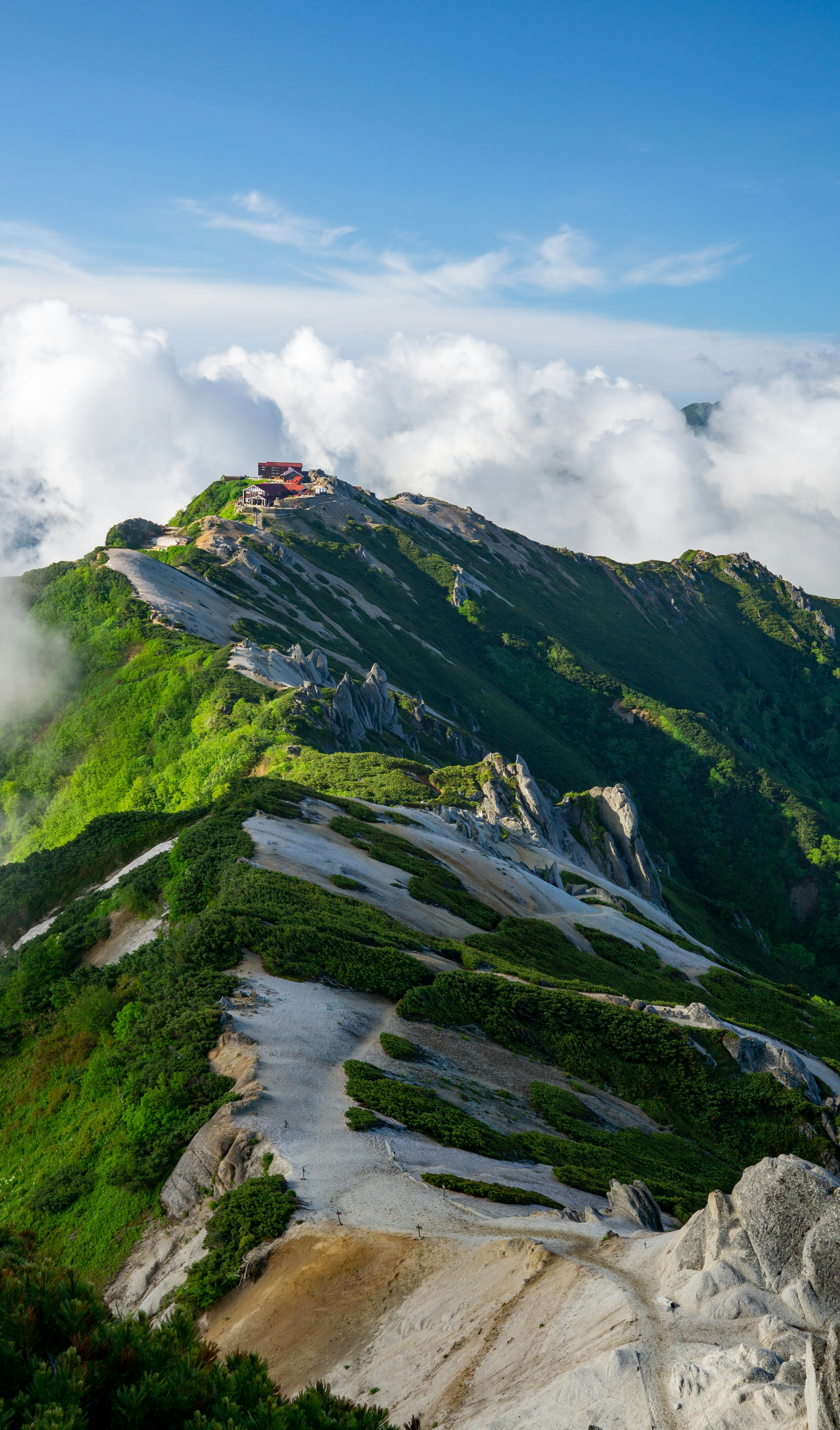 A small building atop a green mountain surrounded by clouds