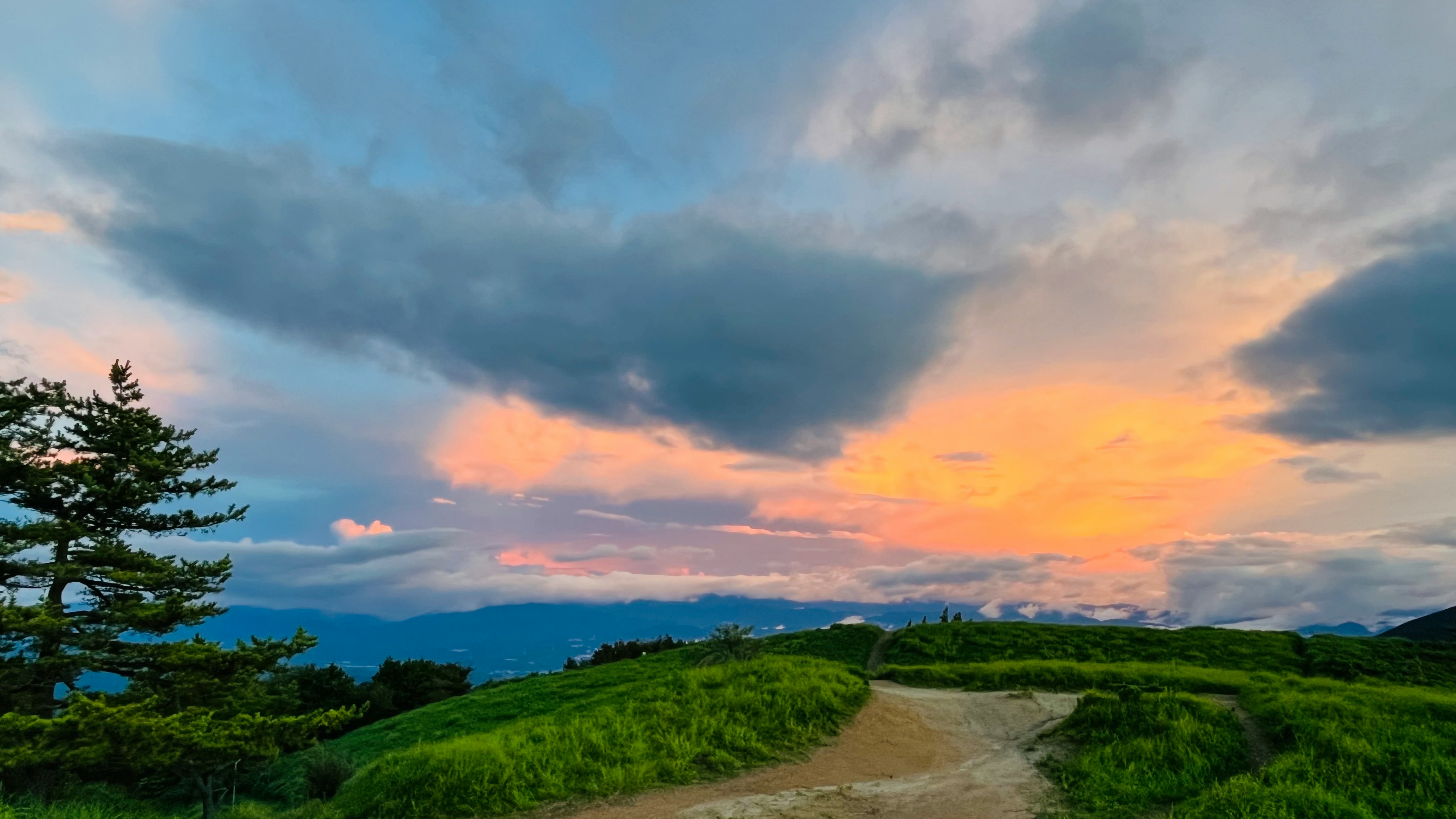 綠色丘陵和藍天的風景 雲朵映襯著橙色的夕陽