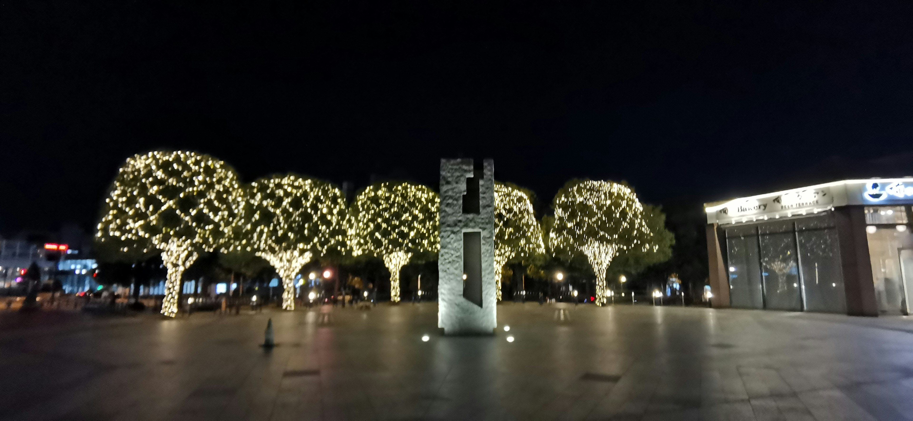 A night scene featuring illuminated trees and a sculpture in a plaza