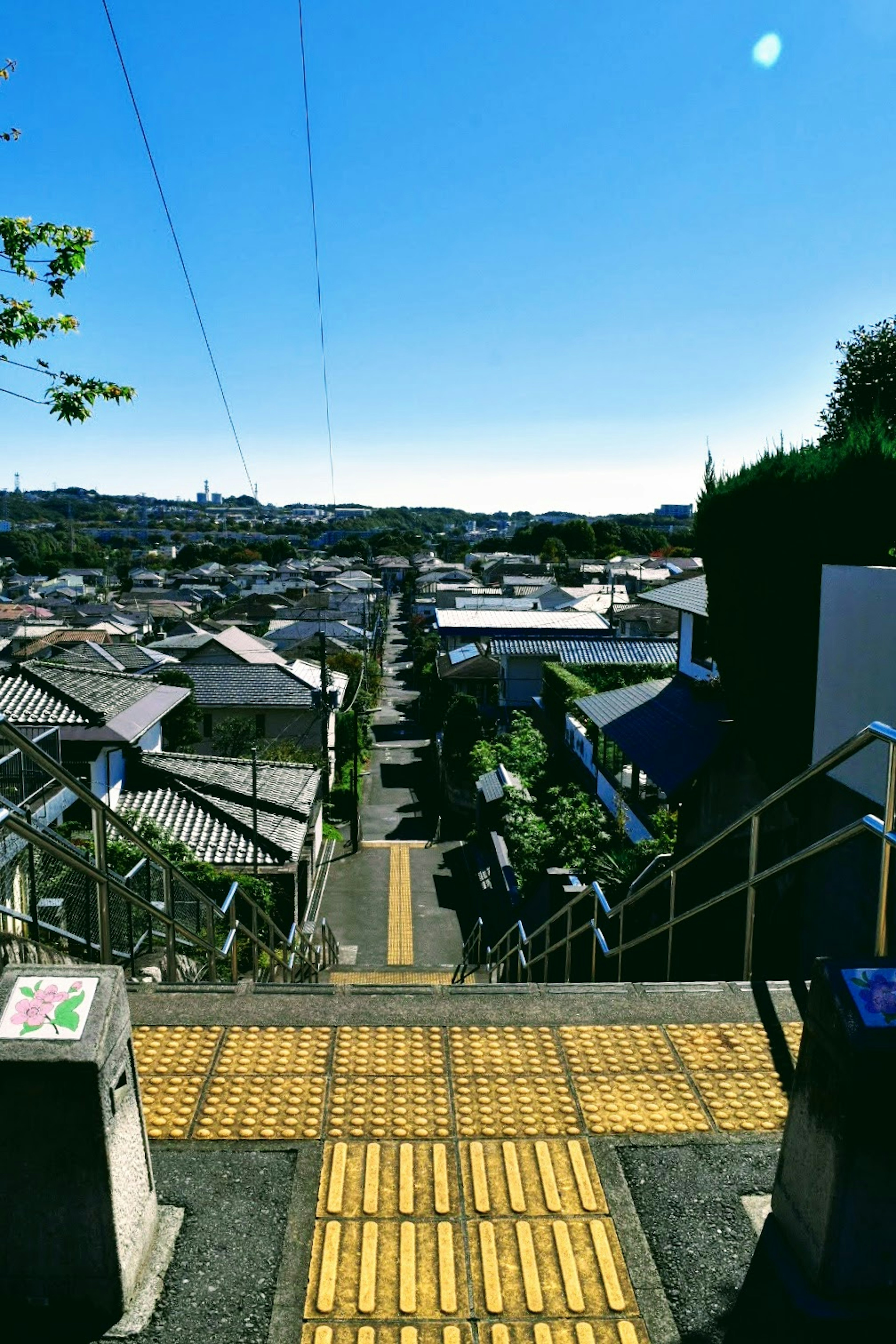 Vista de un área residencial bajo un cielo azul con pavimento táctil amarillo guiando las escaleras