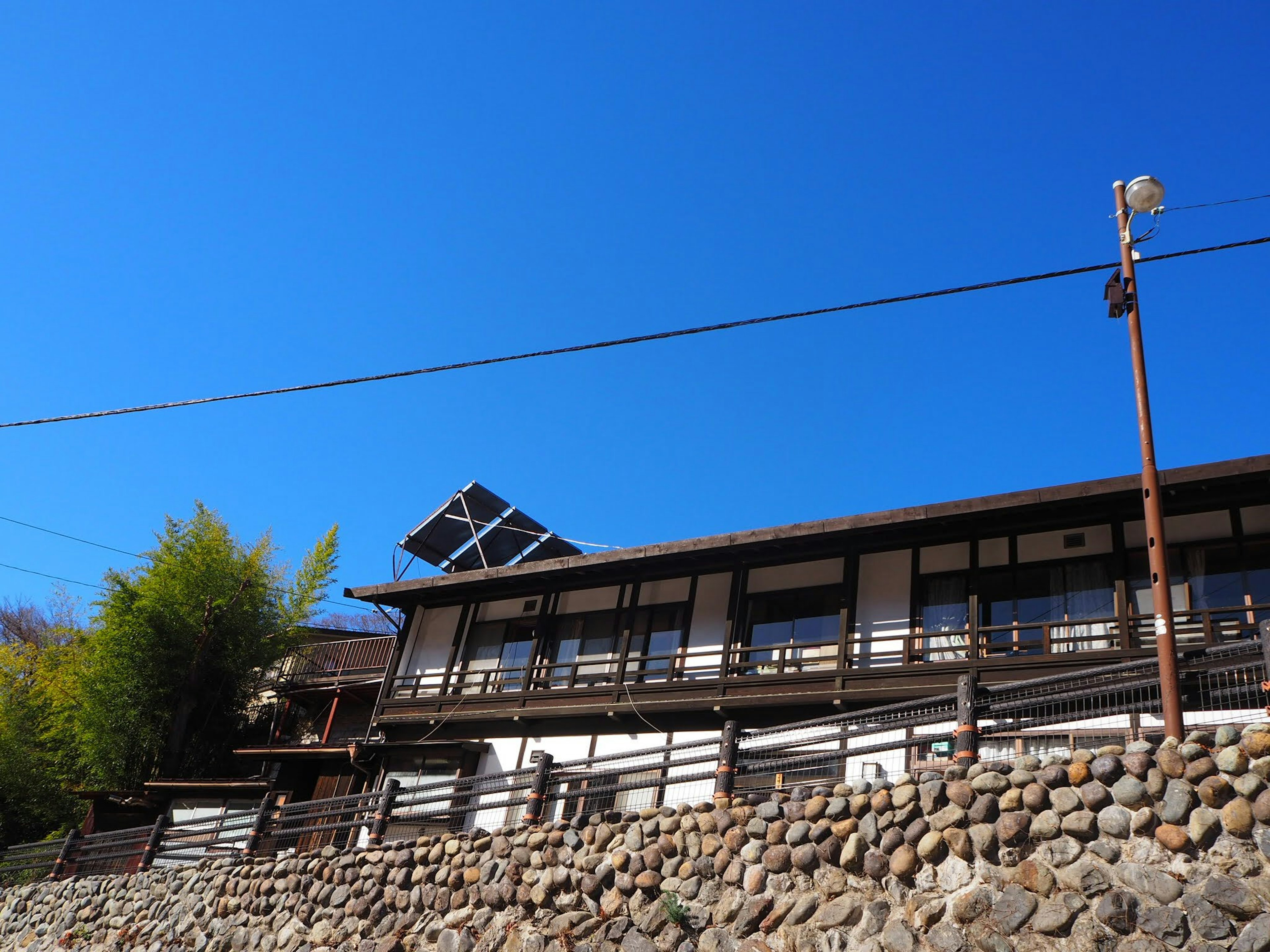 Traditional Japanese house under a blue sky featuring stone wall and bamboo trees