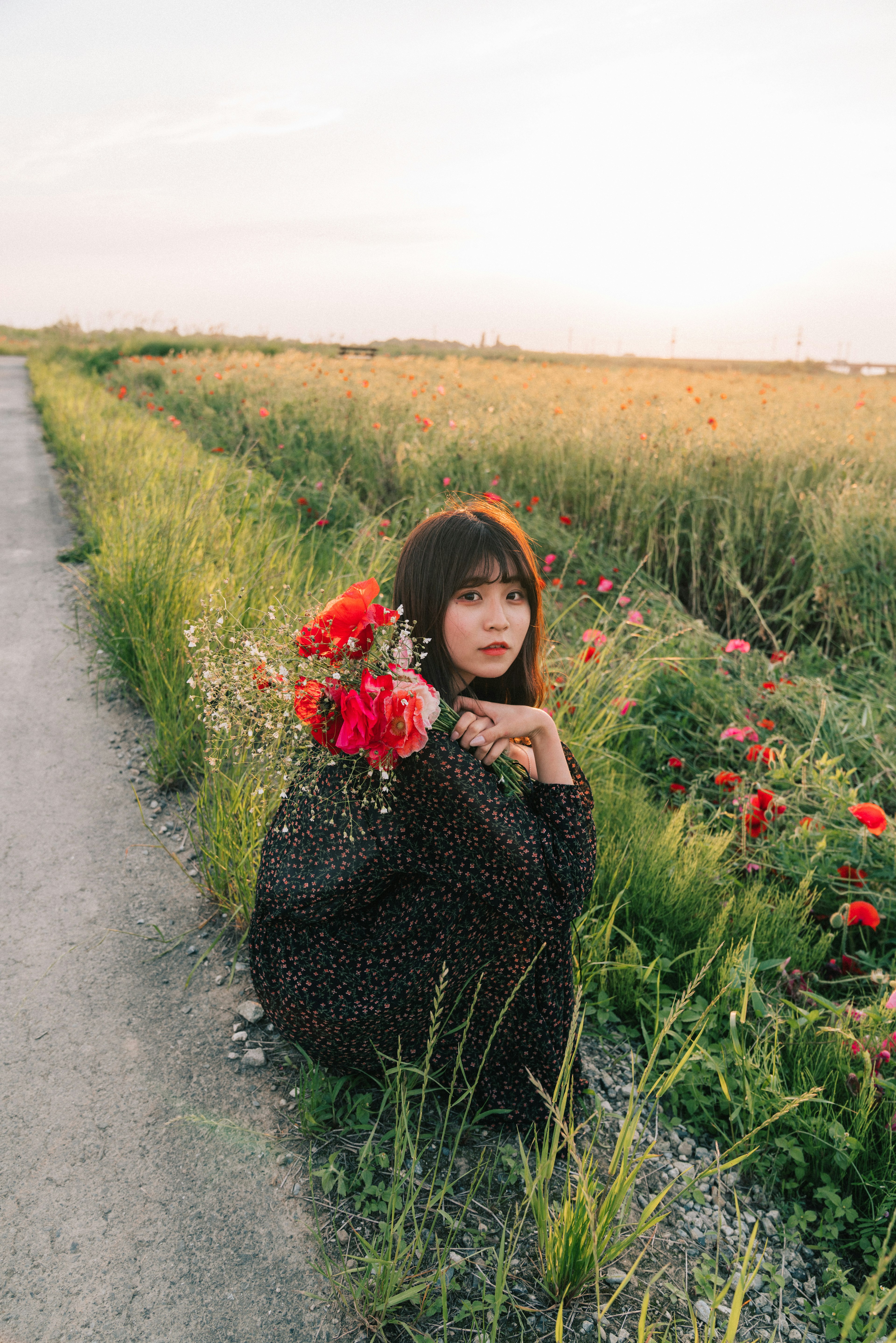 女性が花を持ち草原に座っている風景