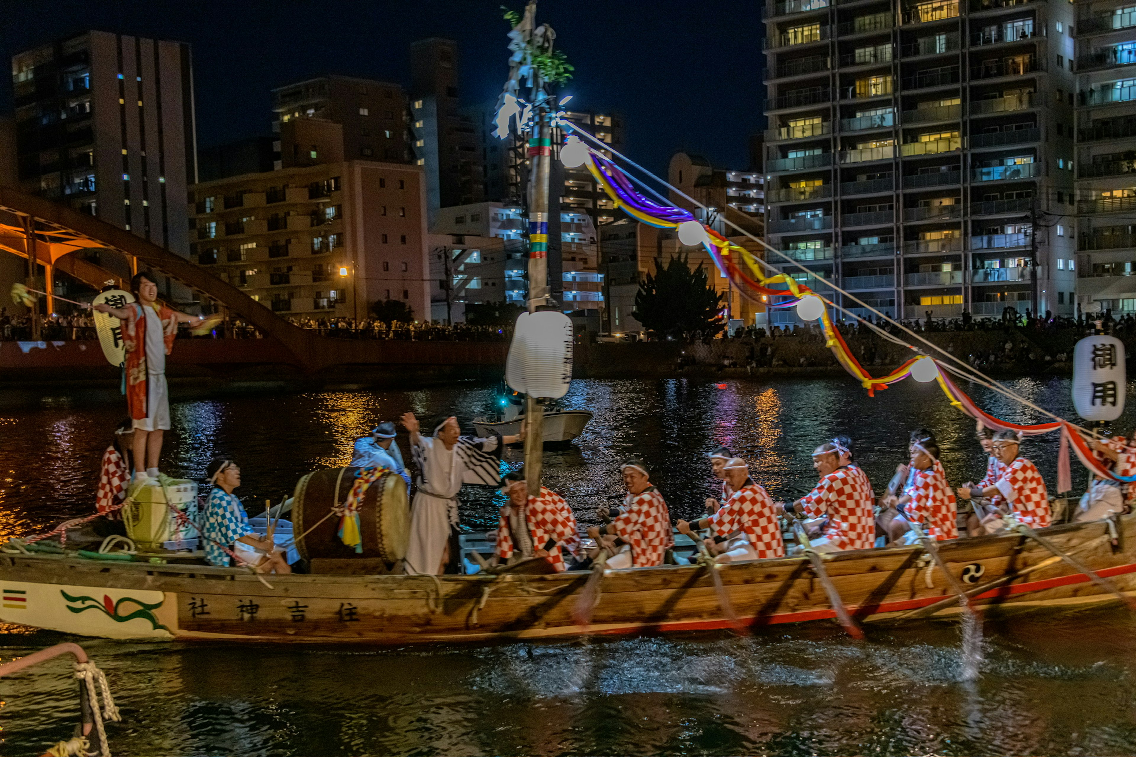 Personas con vestimenta tradicional en un barco festivo navegando por el río de noche