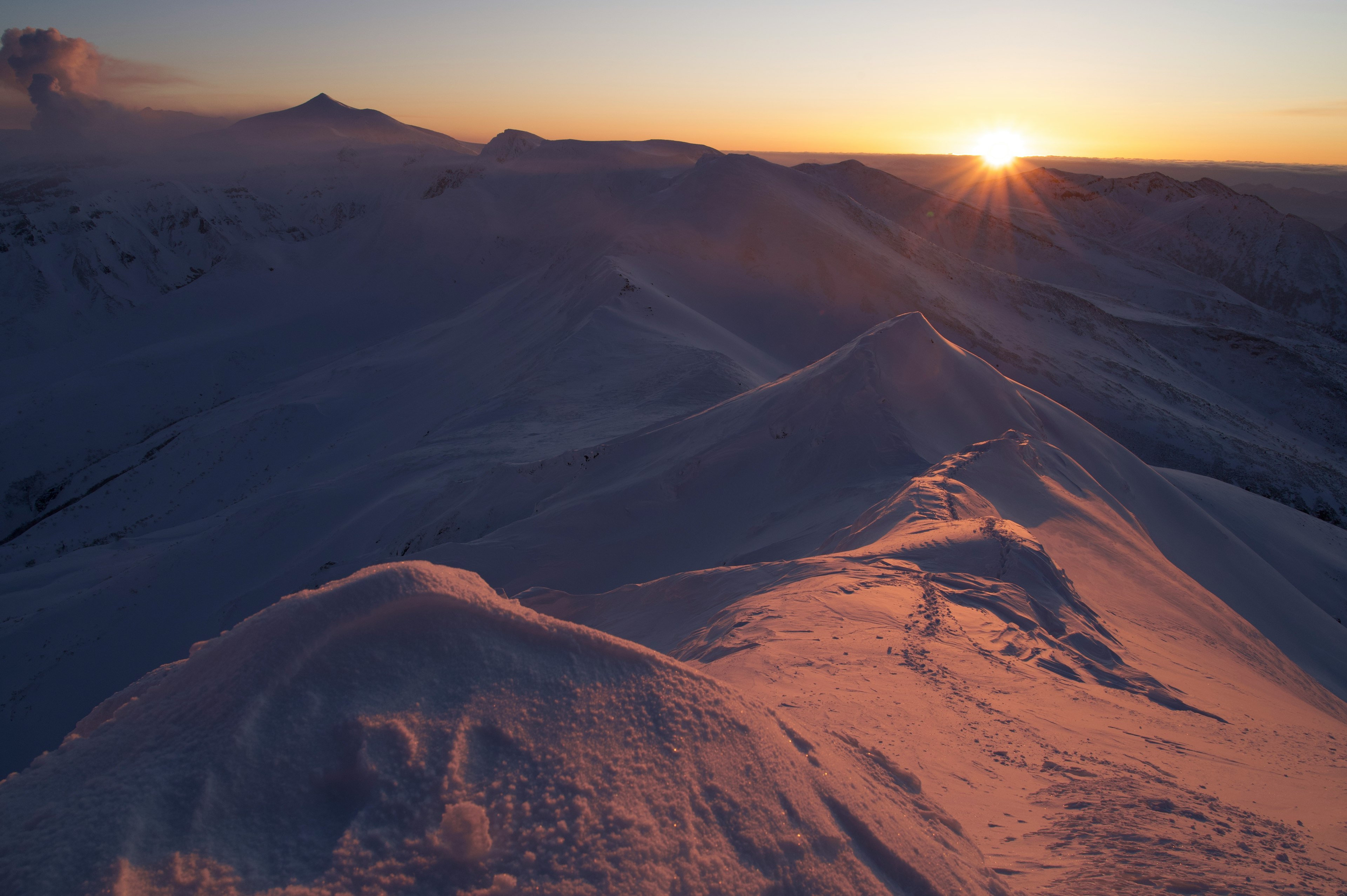 Snow-covered mountains with a rising sun in the background