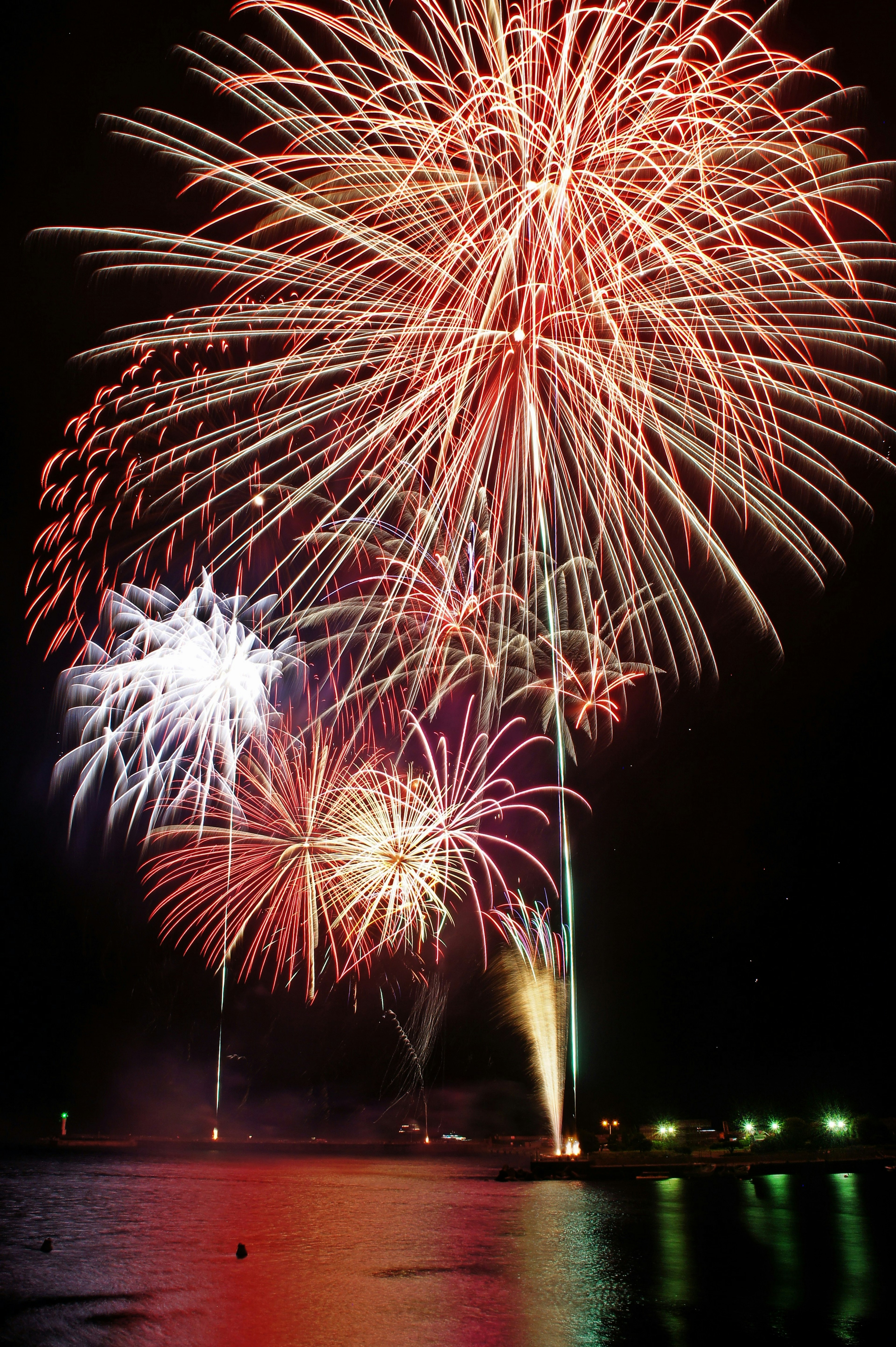 Fuochi d'artificio colorati che esplodono nel cielo notturno riflessi sulla superficie dell'acqua