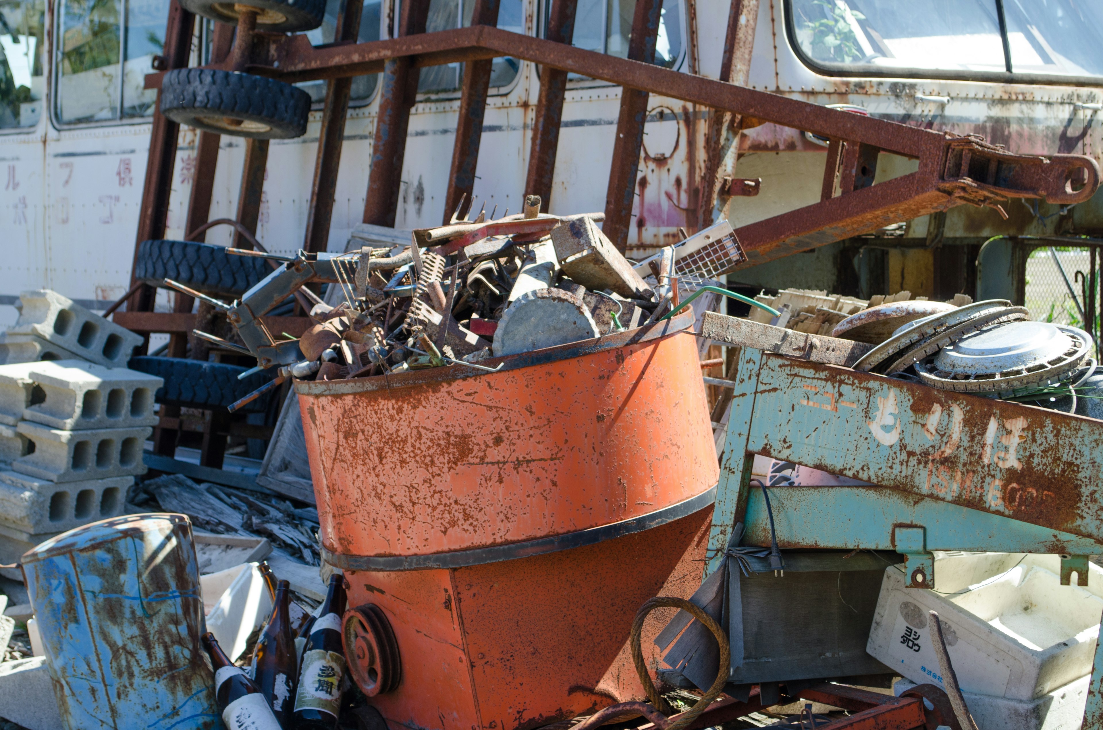 A rusty orange bucket filled with metal scraps and debris in front of an old trailer